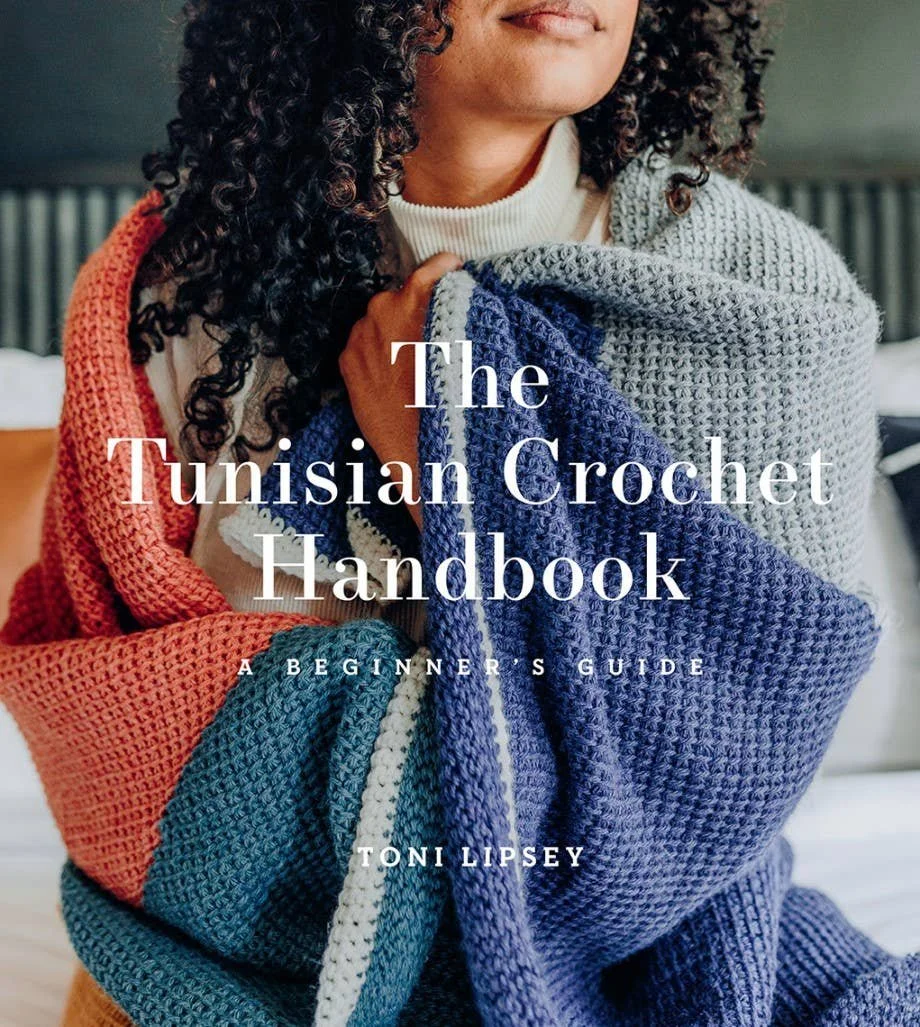 The Tunisian Crochet Handbook on a studio table next to hooks.