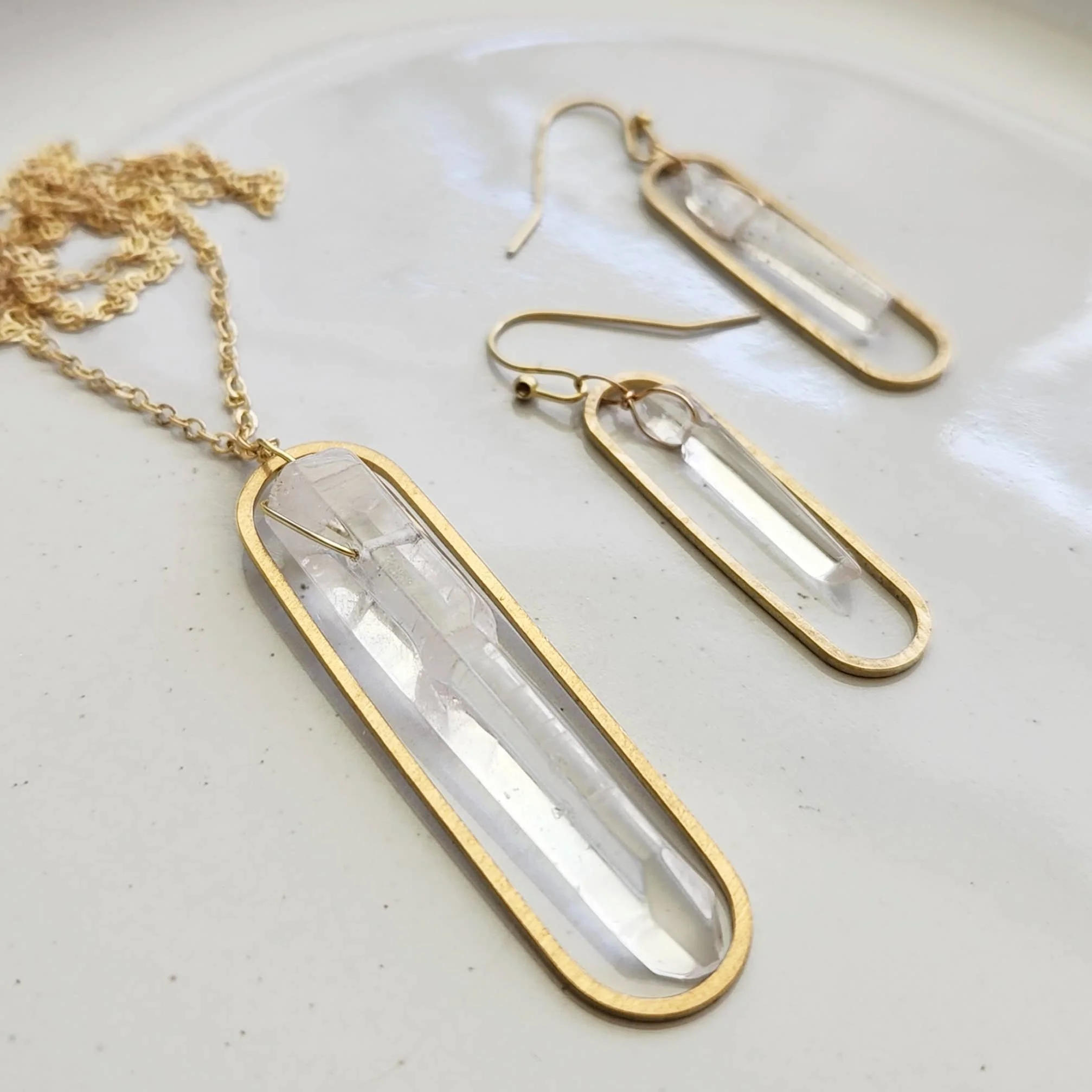 Wire-wrapped clear quartz earrings shown with a matching brass pendant necklace set.