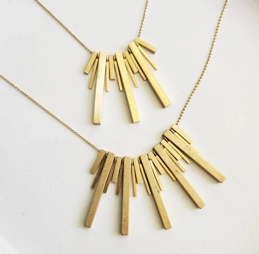 Brass bar necklaces with beaded detail shown in two lengths on a neutral flatlay.