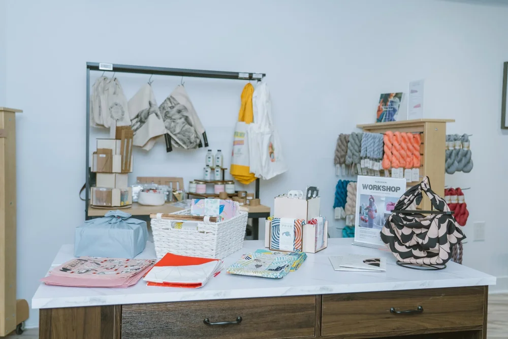 Workshop and merchandise display table at AriYARN Shop and Studio with yarn kits, accessories, and handmade goods.