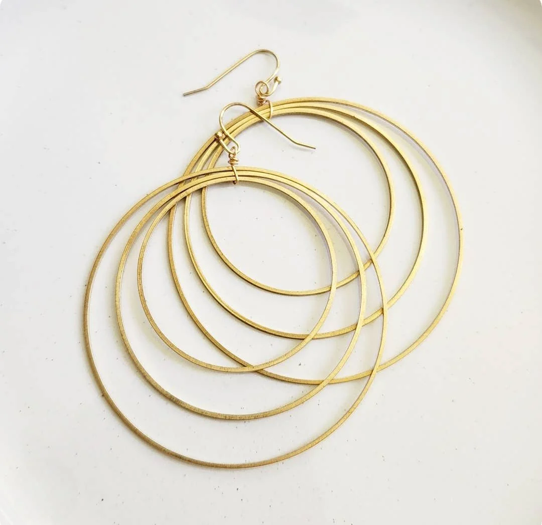 Concentric brass circle dangle earrings with thin hoops on a clean flatlay.