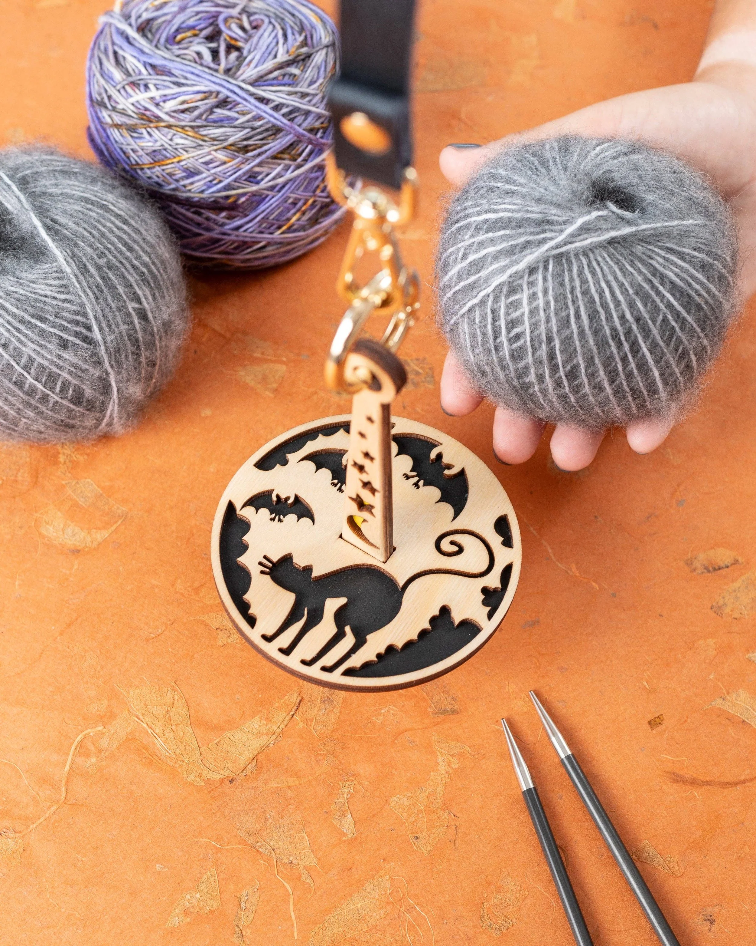 Whimsical wooden cat-bat stitch marker on yarn, Lemonwood-style laser-cut design