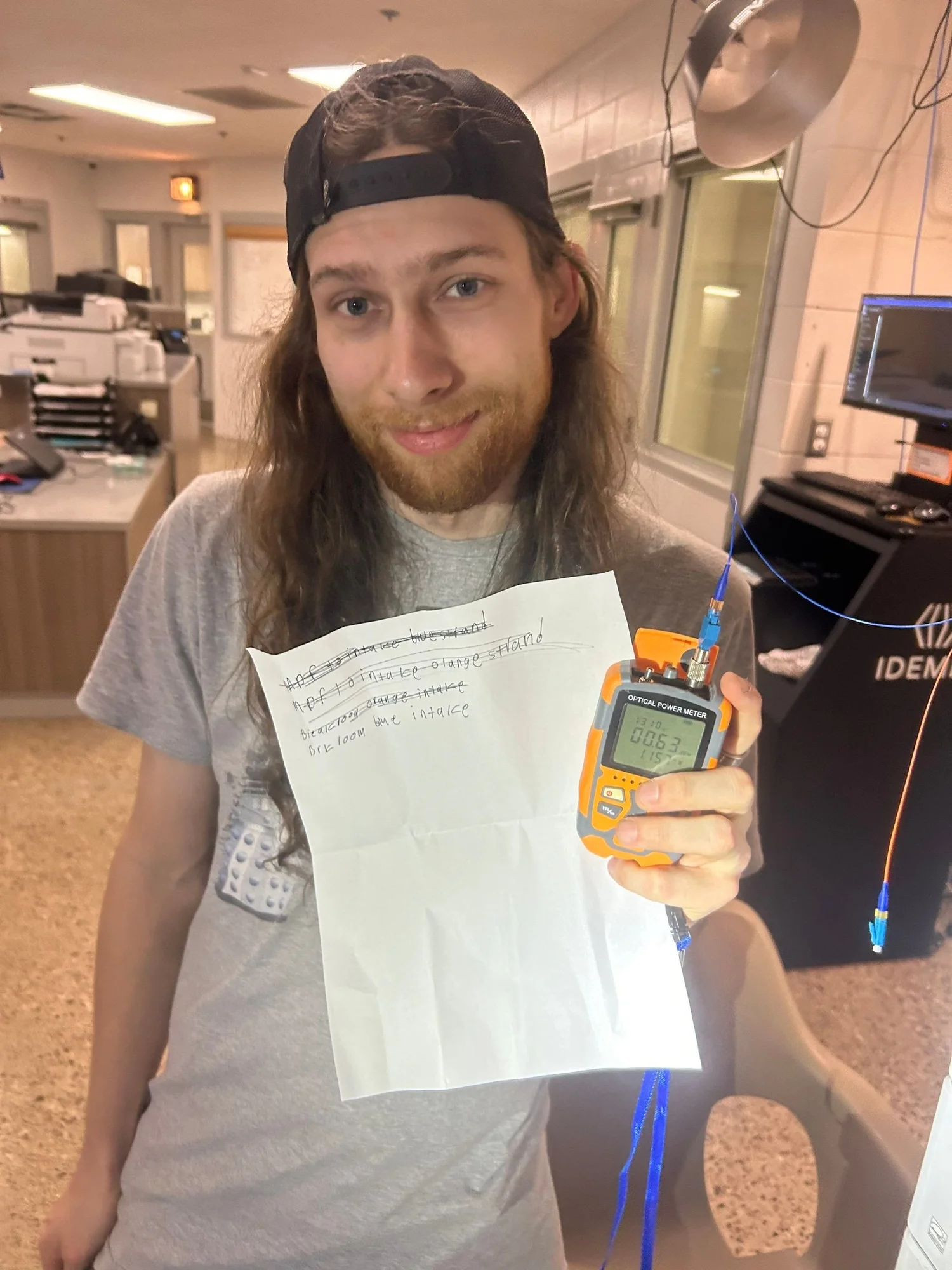 Crispin holding an optical power meter with a 00.63 reading during fiber testing
