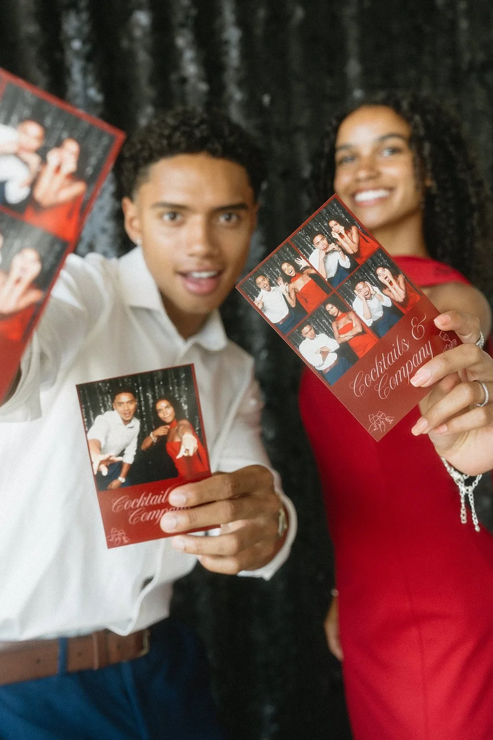 Couple holding their photo booth prints in front of a black sequin backdrop