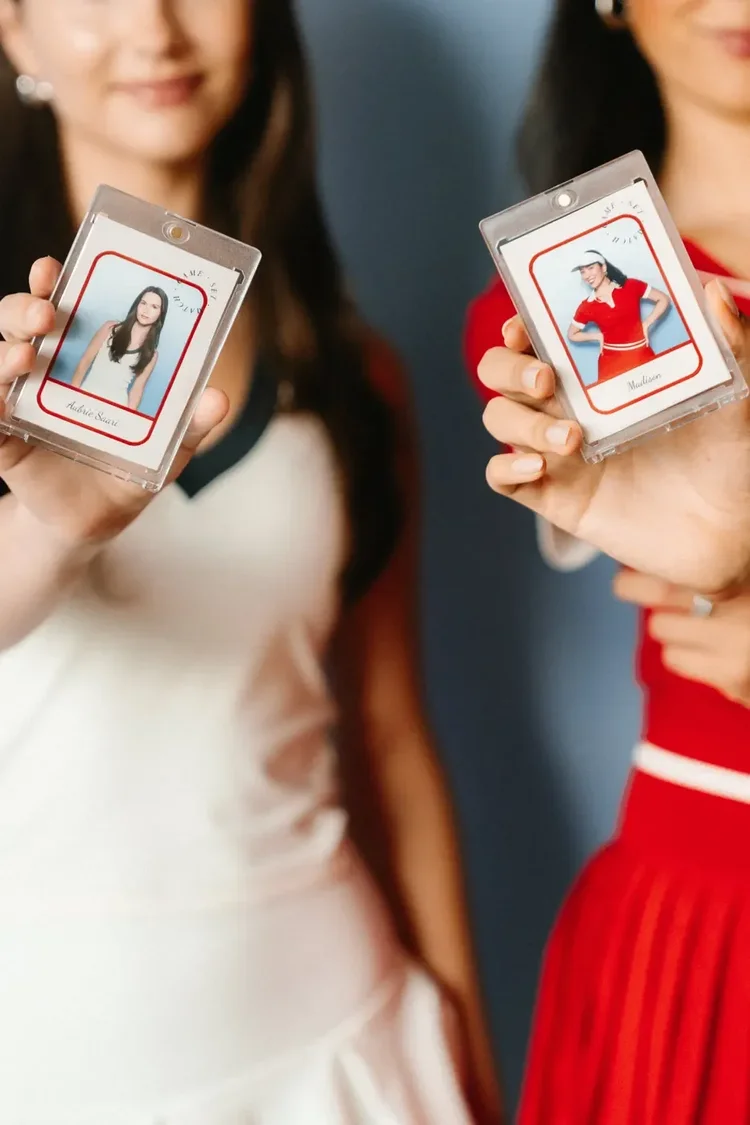 Two guests holding player-card style photo booth prints in clear trading card holders