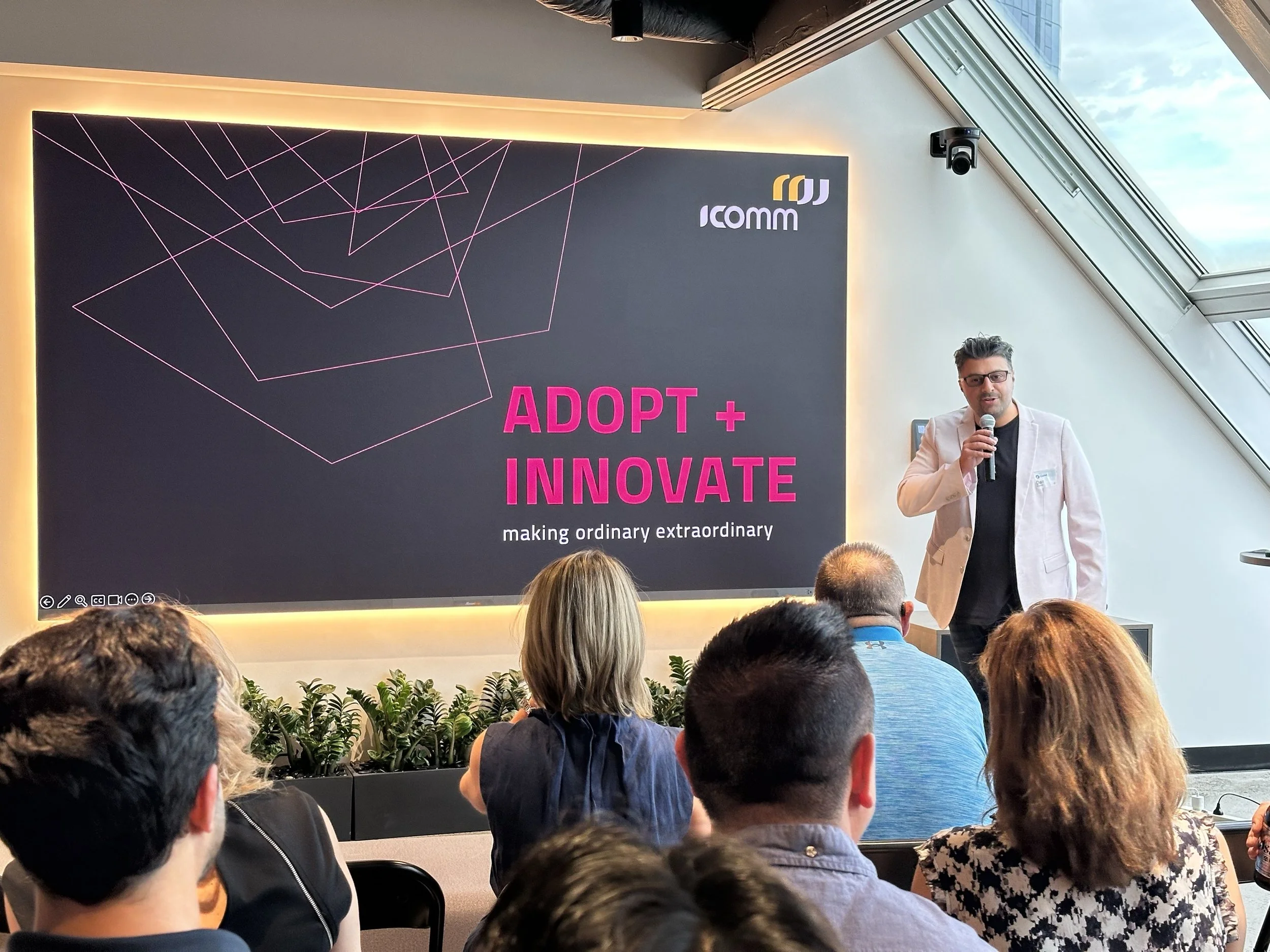 An IComm presenter speaking to an audience in front of an Adopt and Innovate title slide.