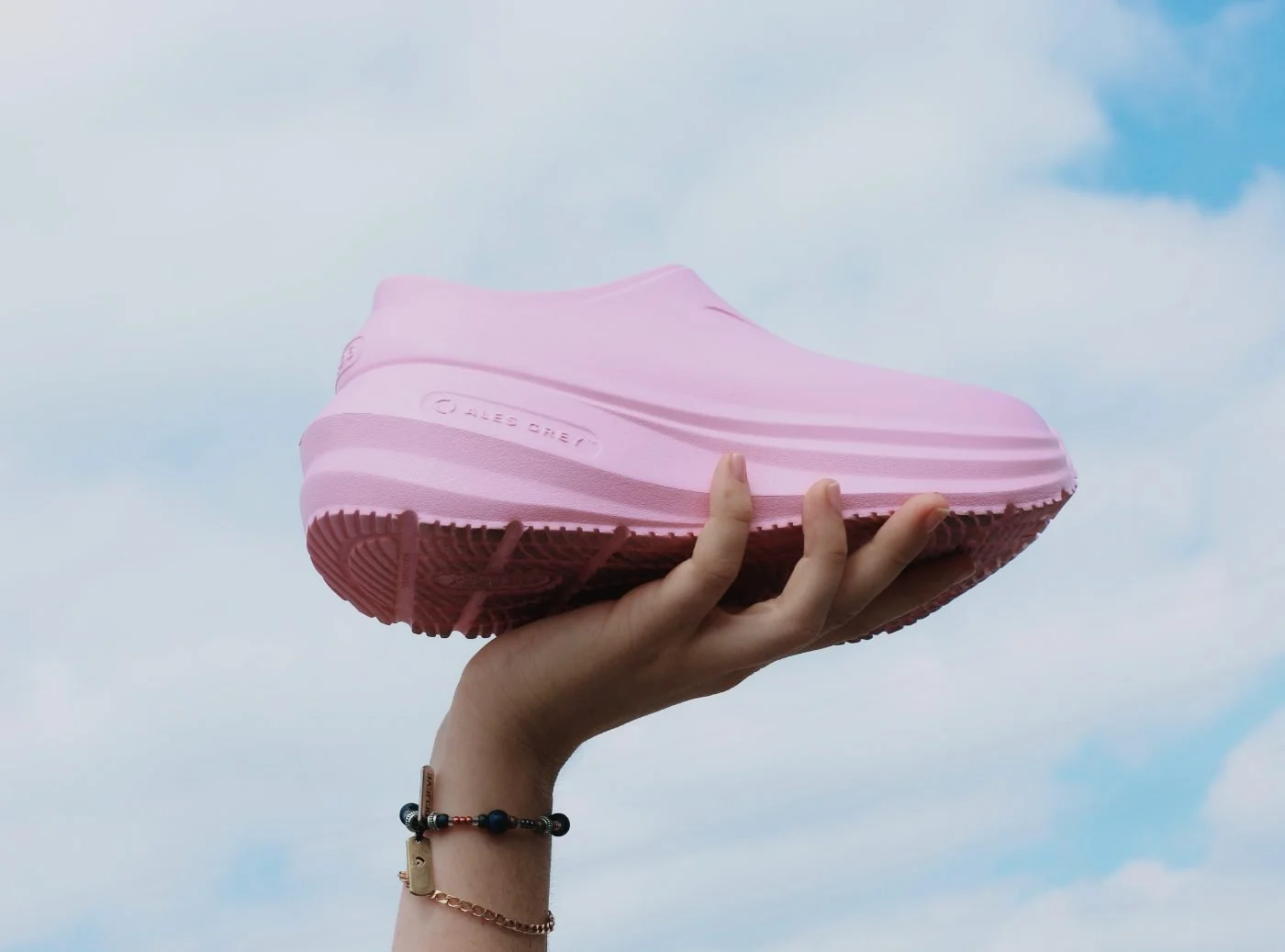 A pink Ales Grey clog held up against the sky