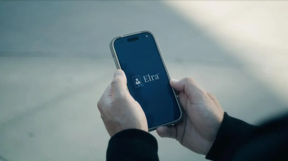 Hands holding a phone showing the Elra app in a film still