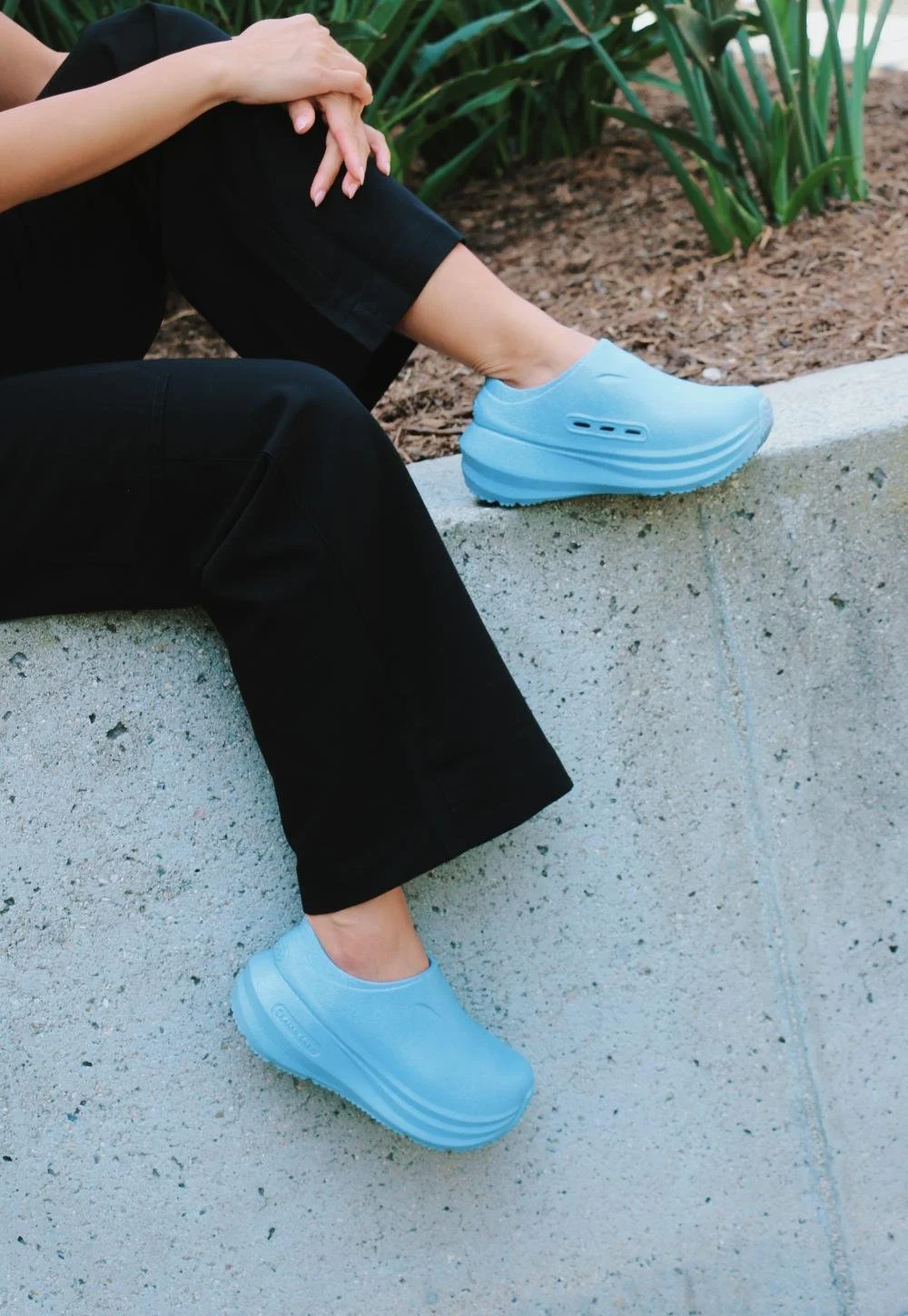 Ales Grey powder blue platform clogs photographed on a concrete ledge