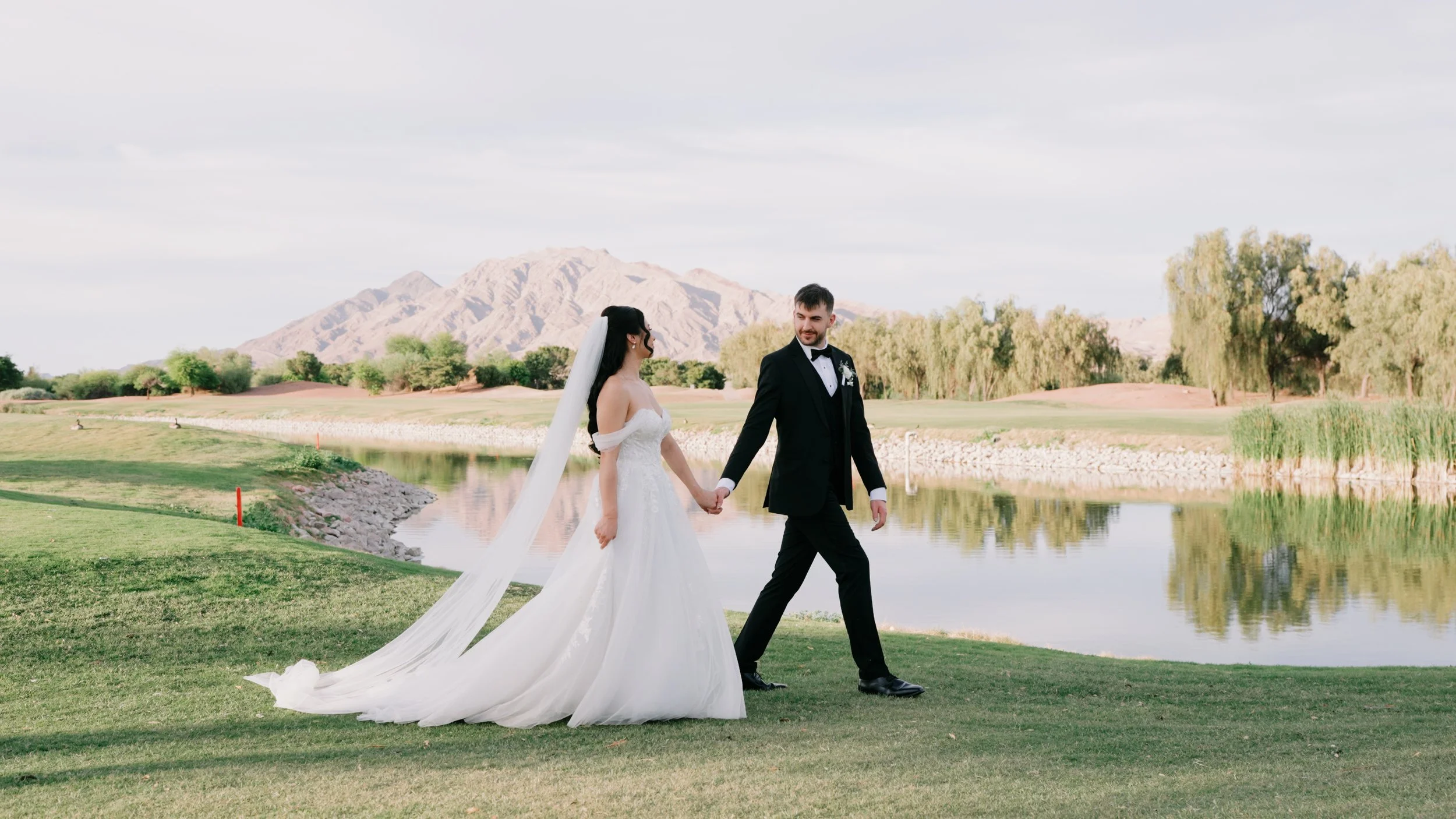 Bride and groom walking hand in hand beside a lake with Las Vegas mountains in the background