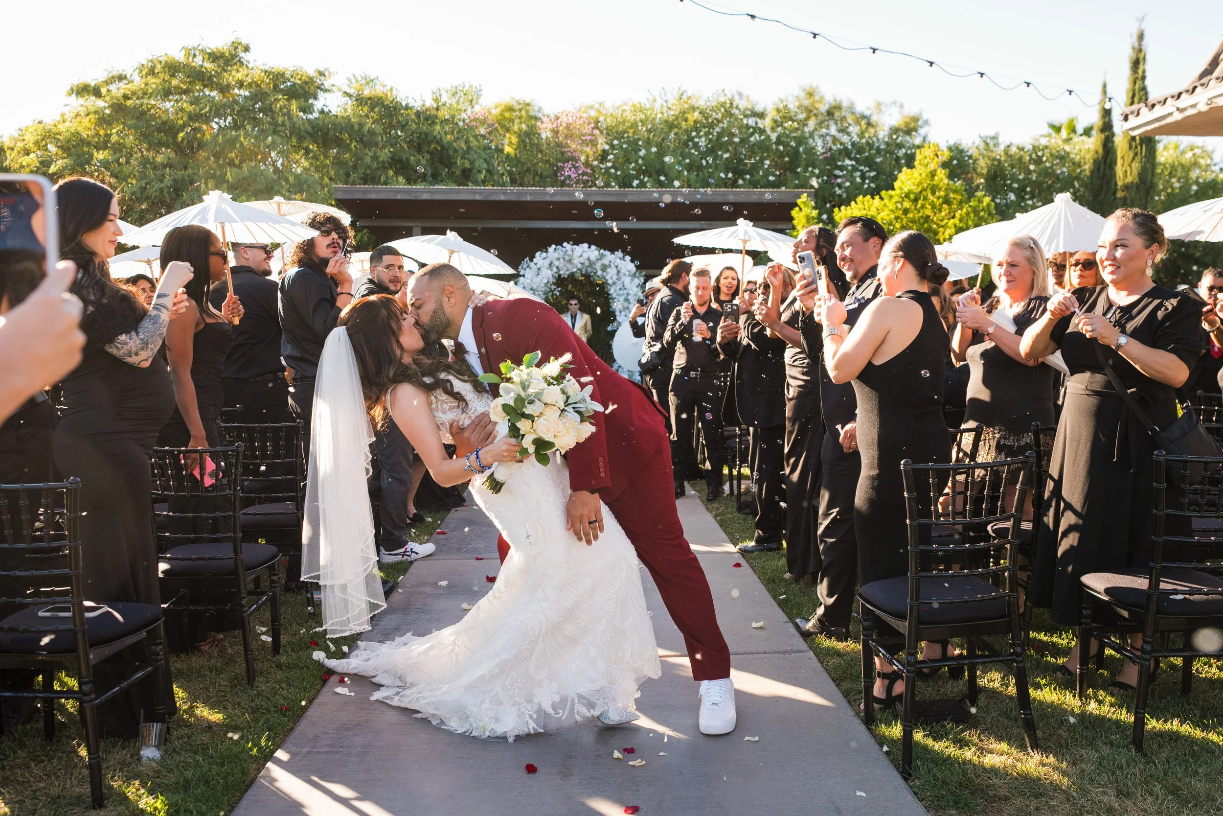 Bride and groom kissing as guests celebrate with bubbles at their ceremony recessional