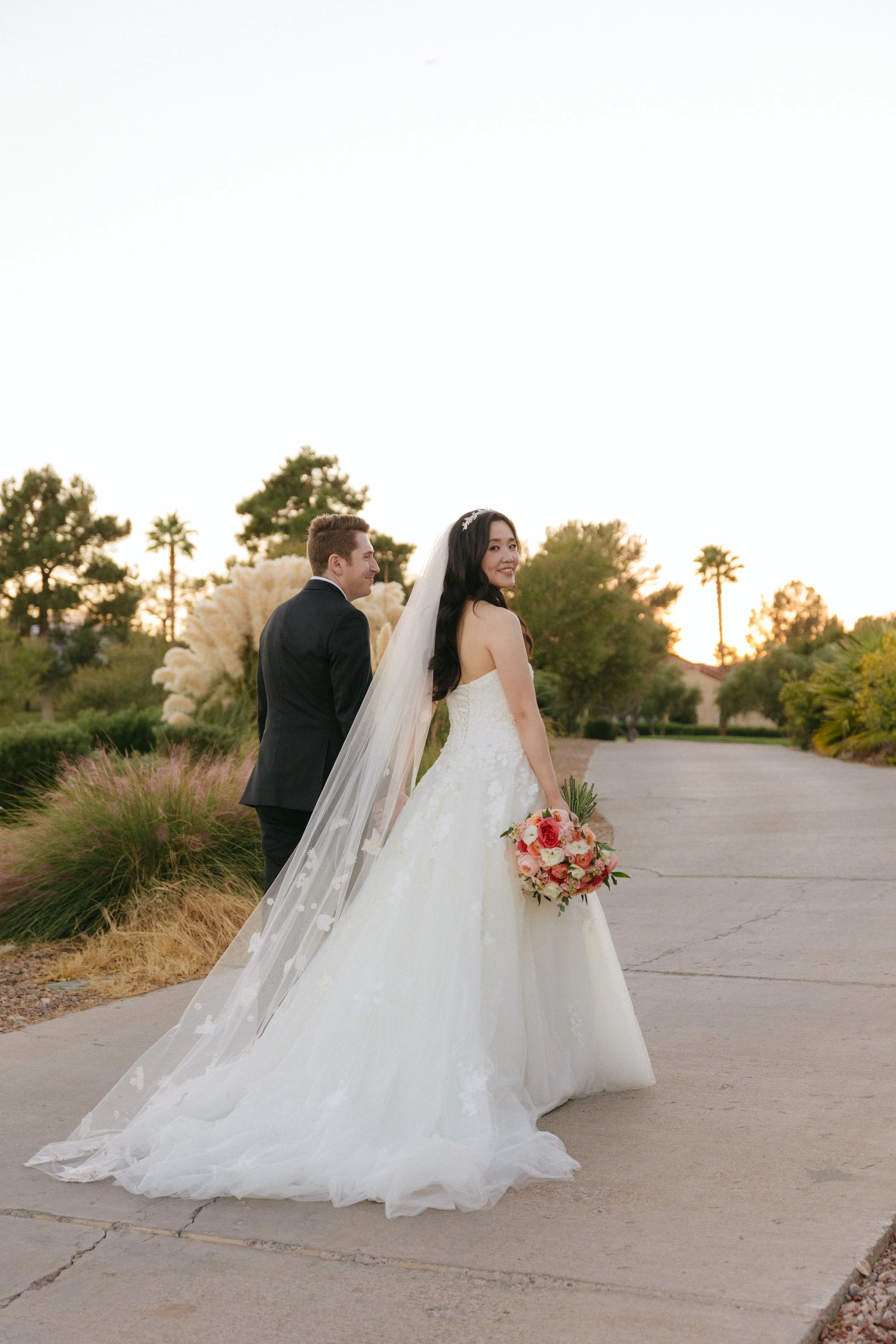 Bride and groom walking together at sunset holding a bouquet