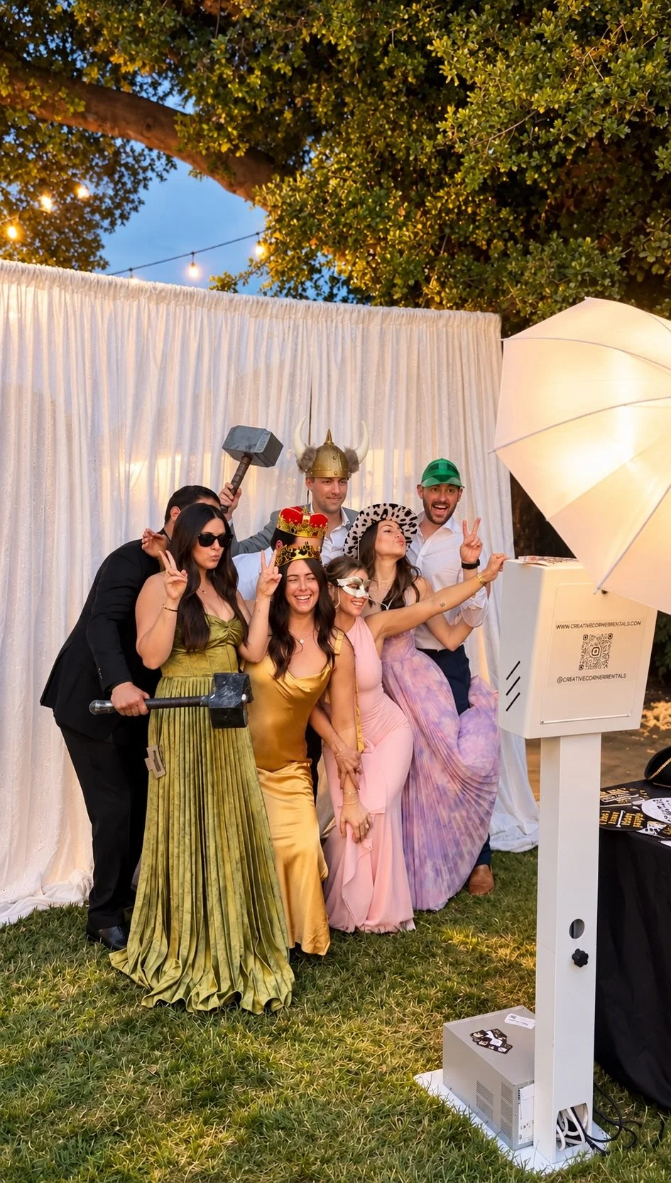 Real wedding guests laughing together and enjoying Creative Corner Rentals Classic Glow photo booth at an outdoor evening celebration