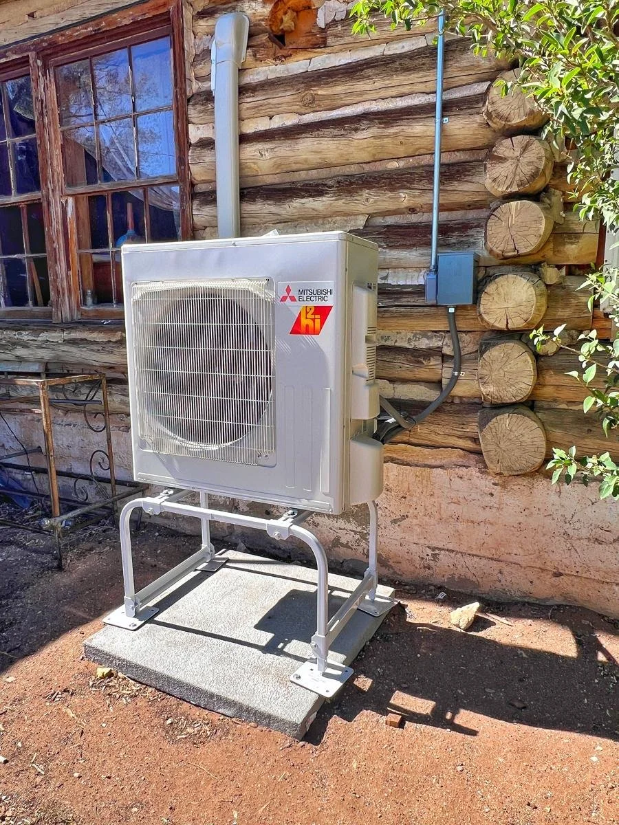 Mitsubishi outdoor unit on a stand beside a log cabin wall