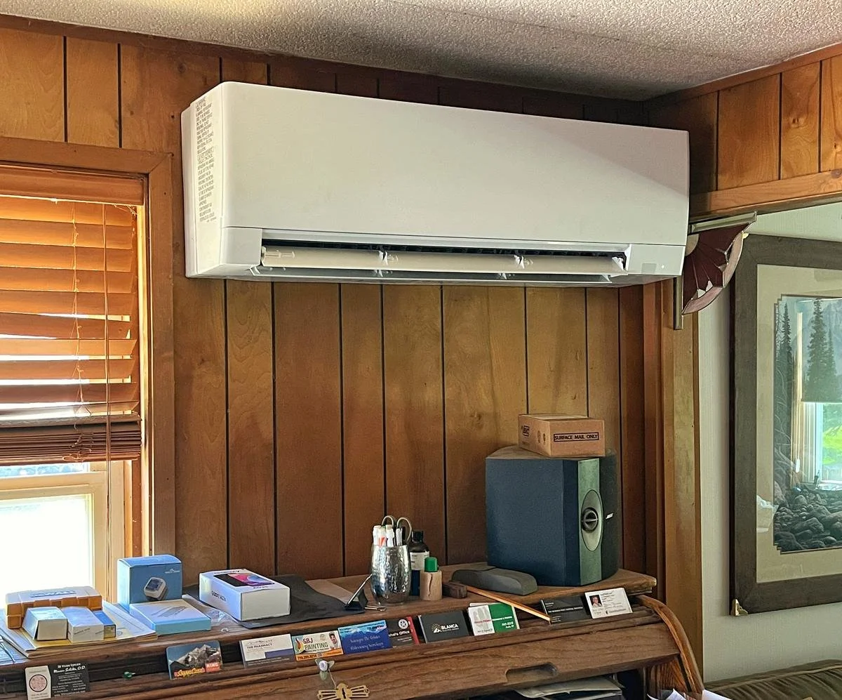 Wall-mounted Mitsubishi indoor unit in a wood-paneled room above a desk