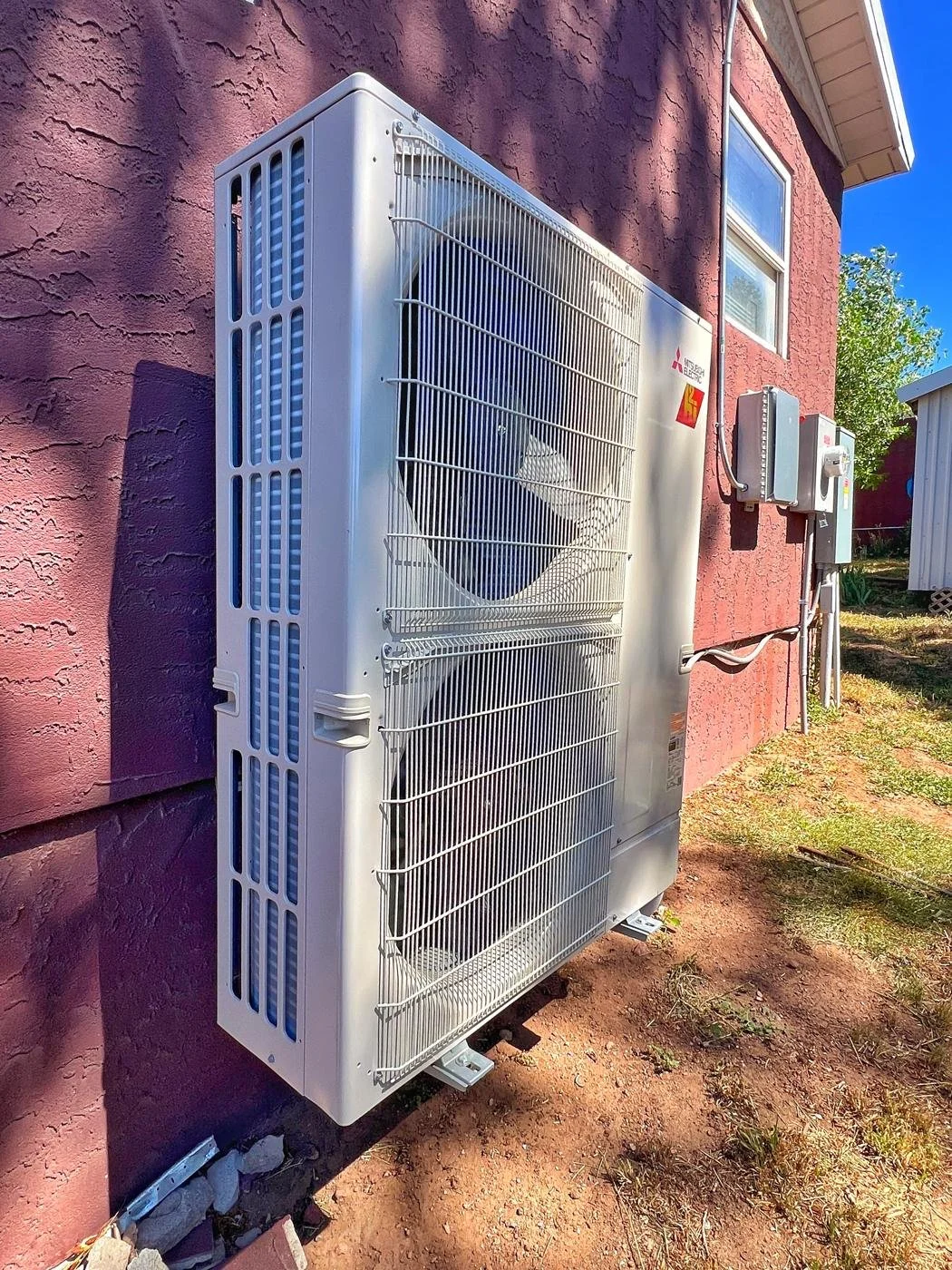Tall Mitsubishi outdoor unit beside a red stucco house