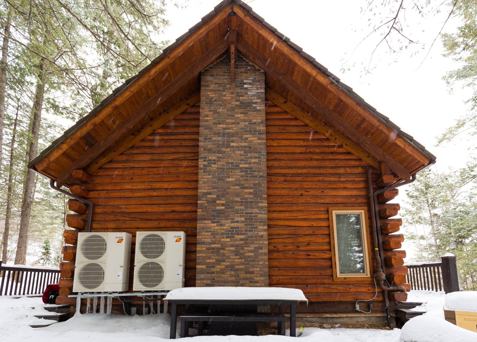 Log cabin in fresh snow with two Mitsubishi outdoor heat pump units beside it