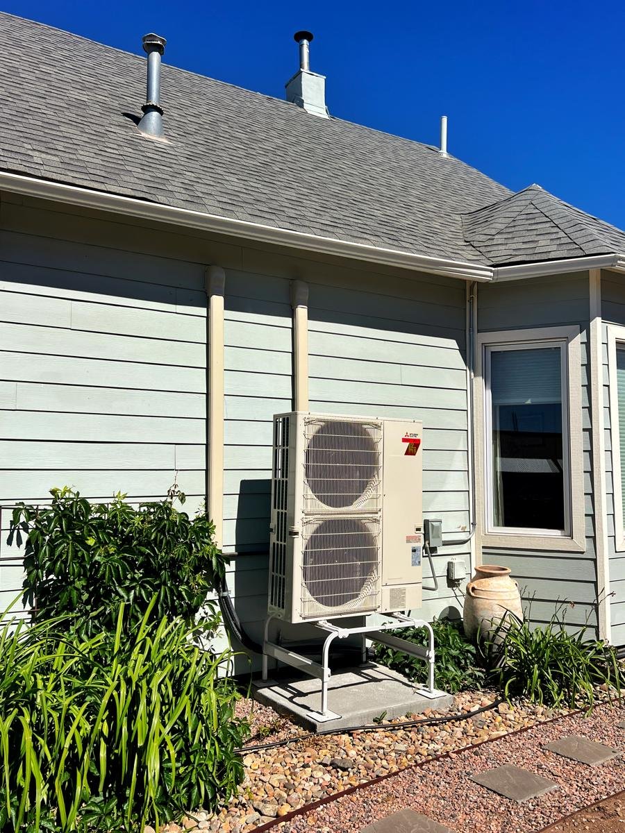 Mitsubishi outdoor unit on a stand beside a blue-gray house