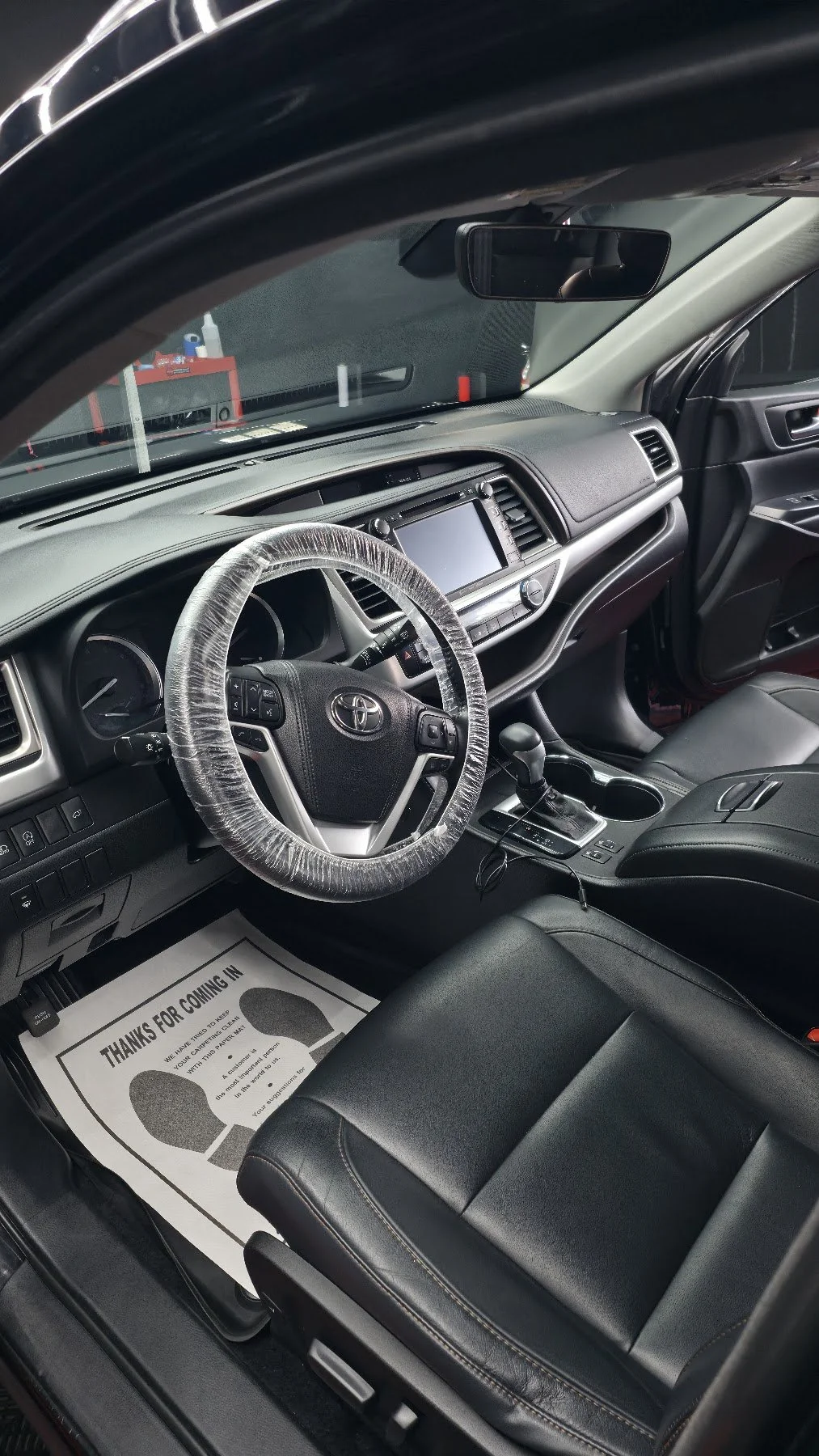 Clean Toyota interior with protected steering wheel, black seats, and a paper floor mat