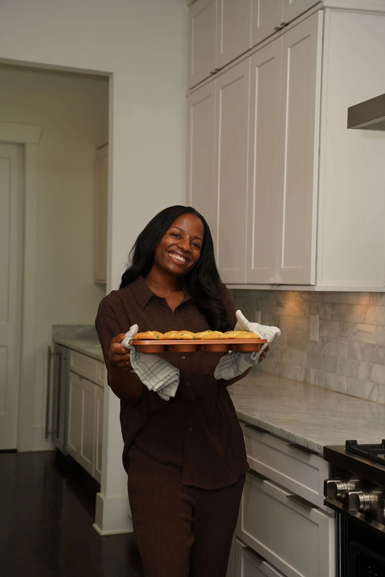 Briana smiling in her kitchen while holding a tray of freshly baked cupcakes