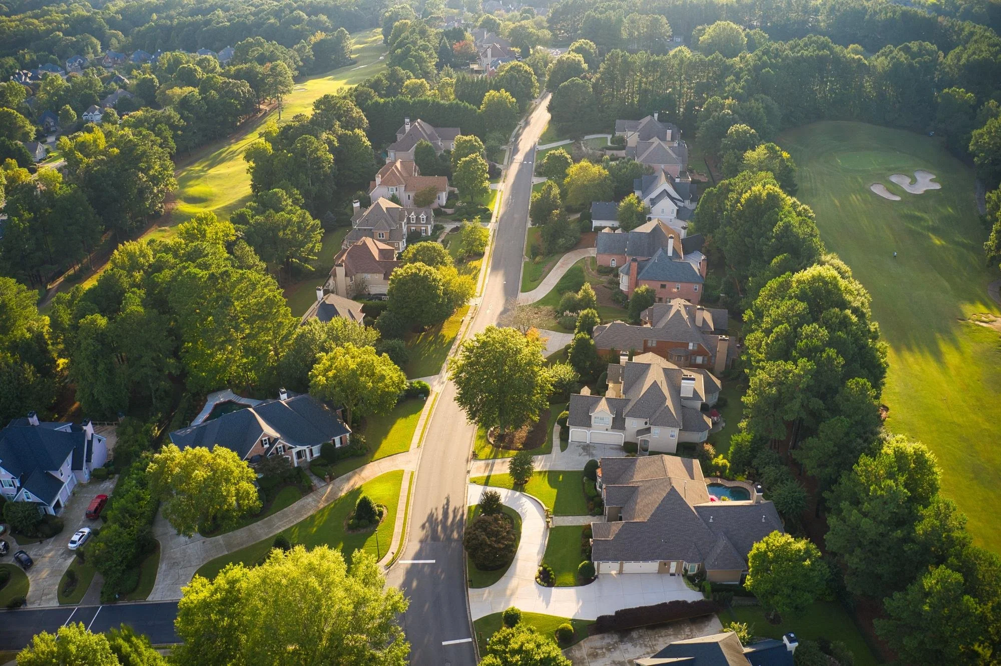 Aerial view of a tree-lined neighborhood beside a golf course at golden hour