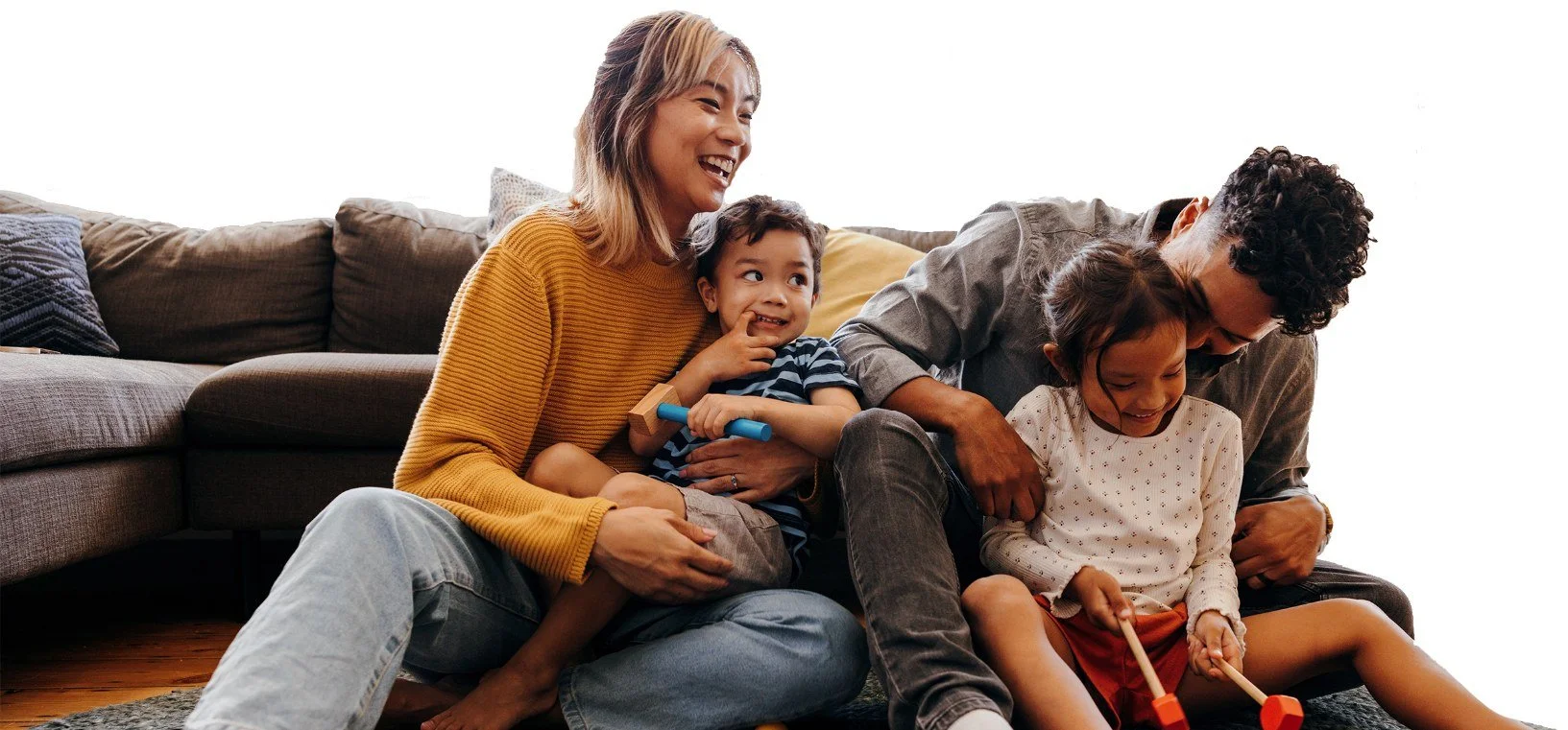 A mother and father laughing with their son and daughter on the living room floor