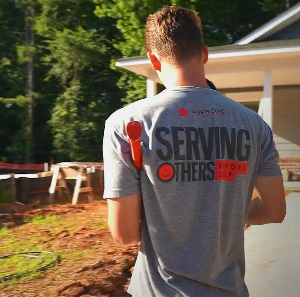 A Supreme Lending volunteer in a Serving Others Before Self shirt walks toward a newly built home