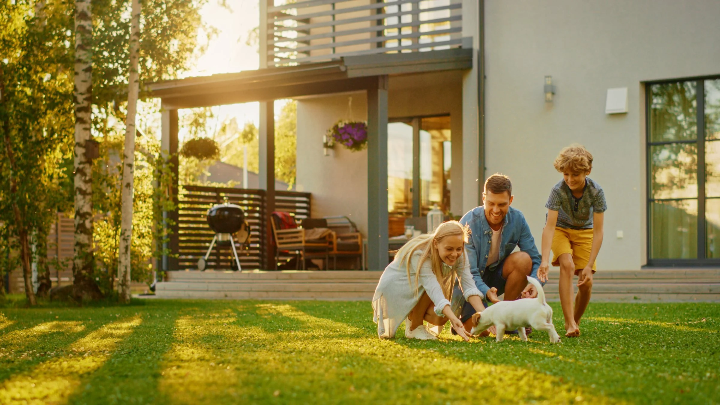 A family plays with their puppy on the lawn behind their home at golden hour