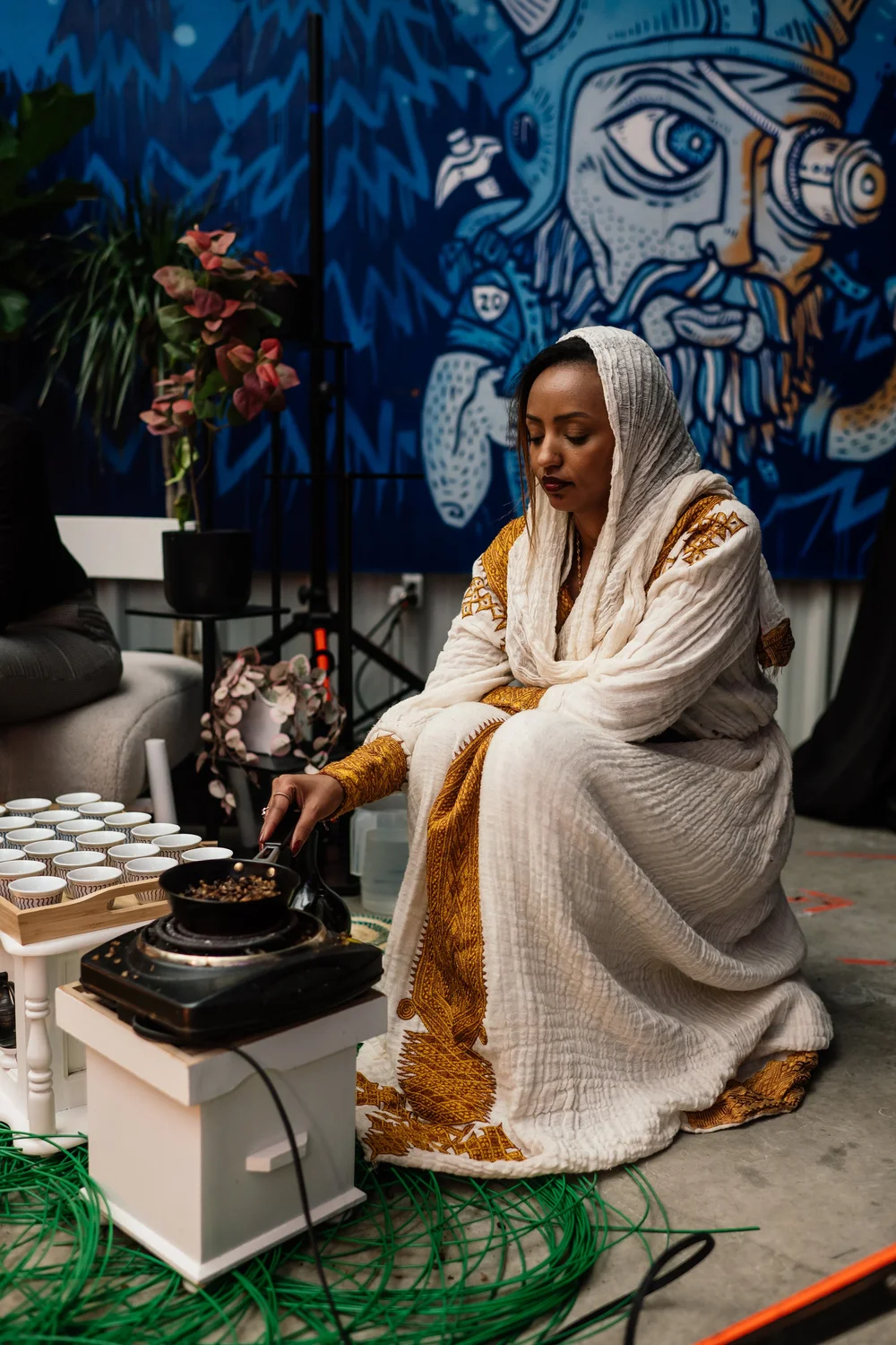 Luwam in a white and gold dress leading a coffee ceremony
