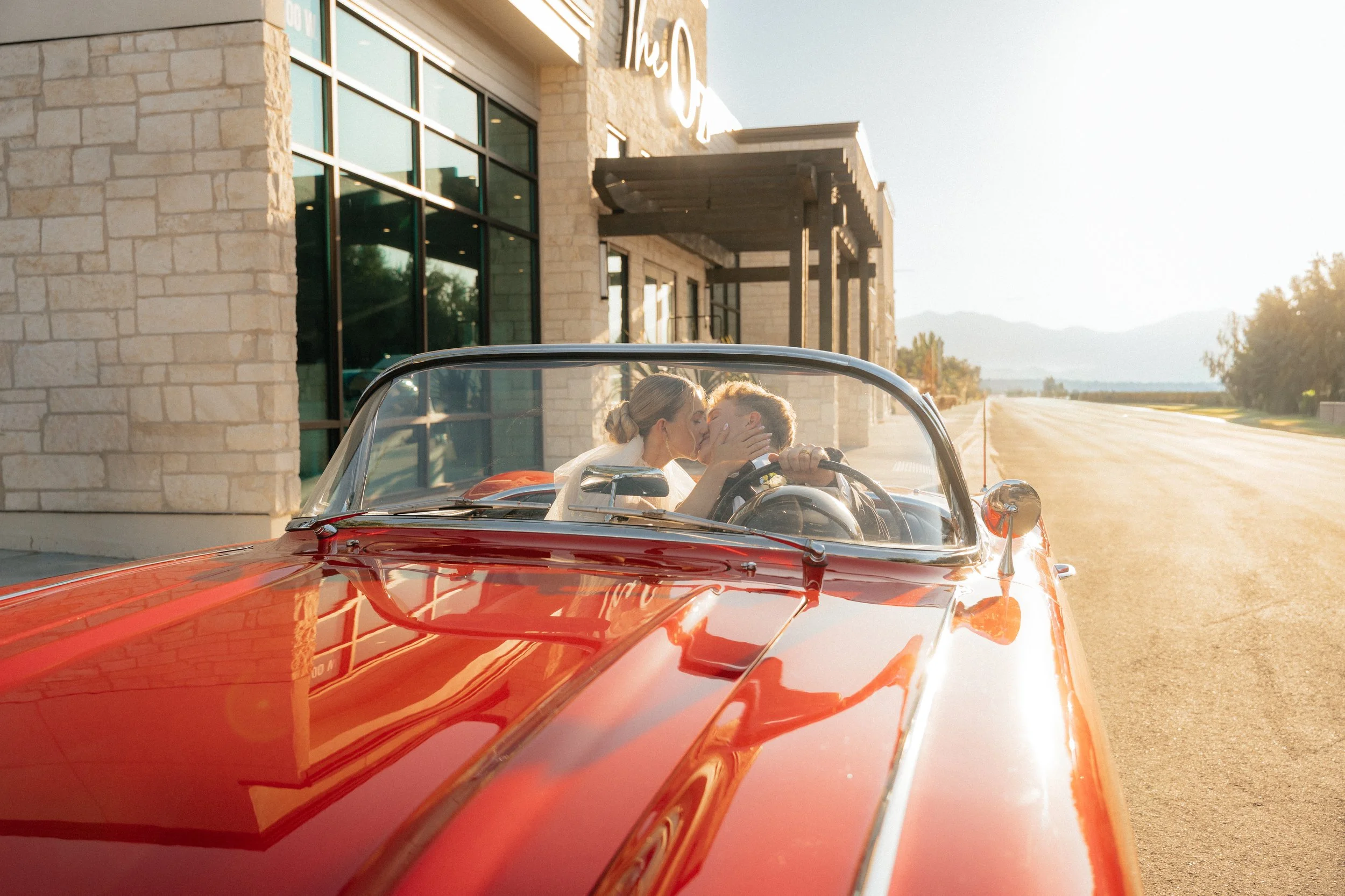 Newlyweds share a kiss in a red convertible outside The Oz in Lehi, Utah