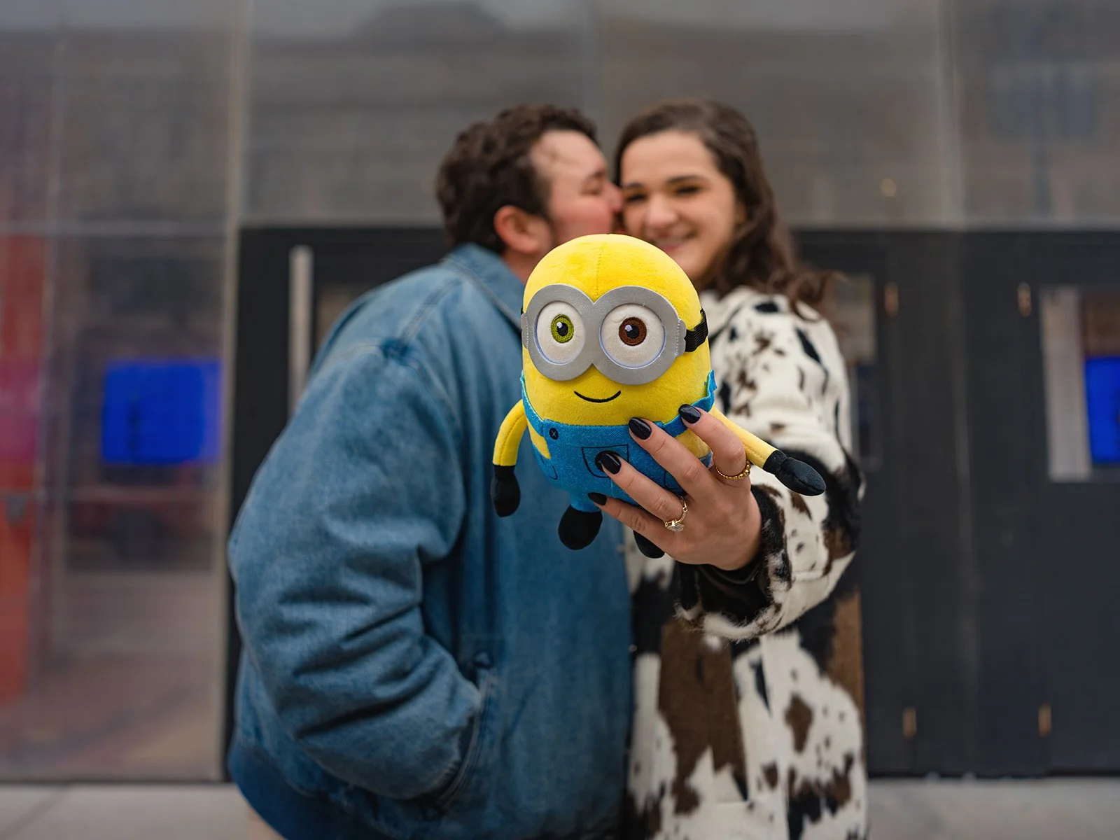Engaged couple kissing behind a Minions stuffed animal at the Davis Theater in Lincoln Square, a callback to their first date movie