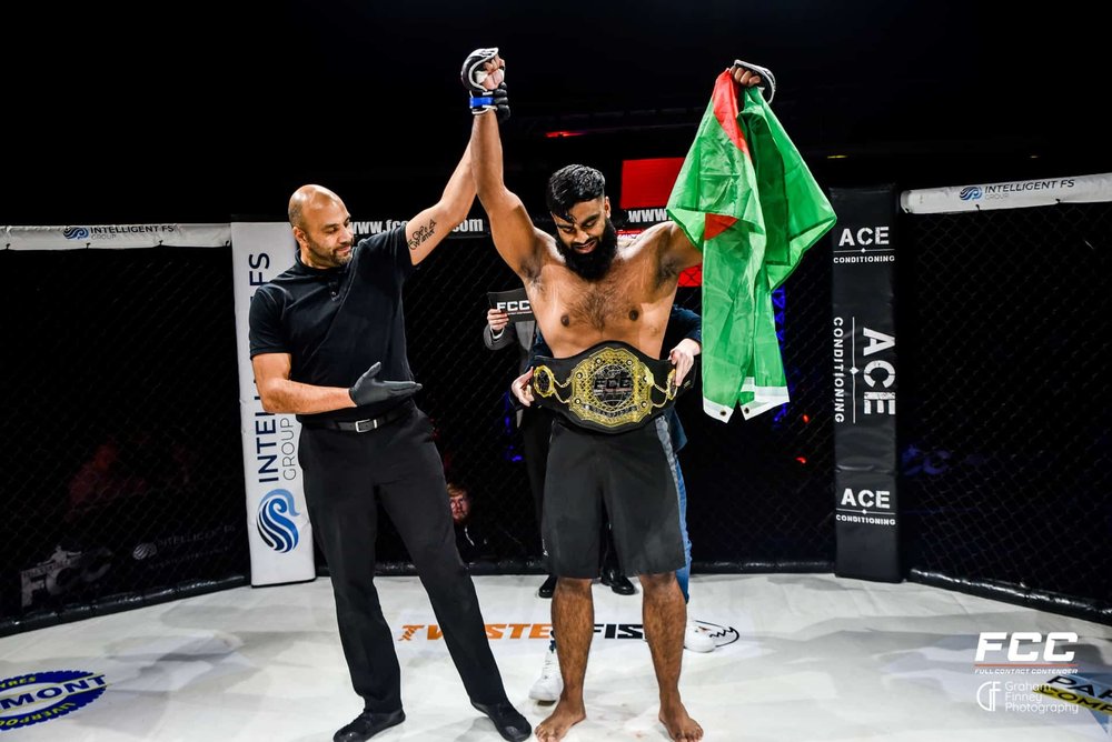 Tigerstyle head coach with his arm raised and the championship belt after winning at FCC