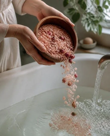 Hands pouring pink bath salts and rose buds into running water