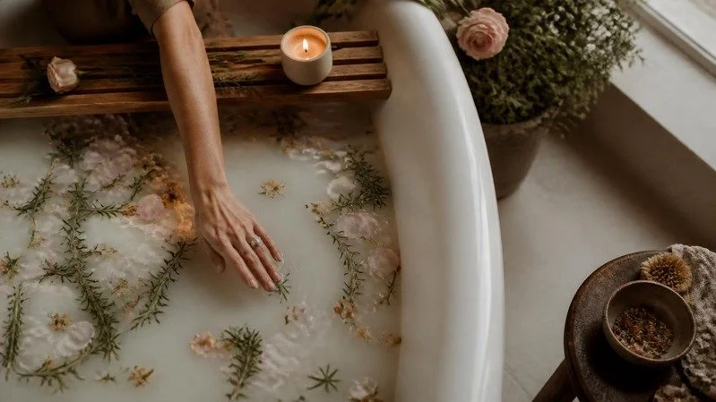 Hands resting in a ritual bath of warm water, rosemary and rose petals
