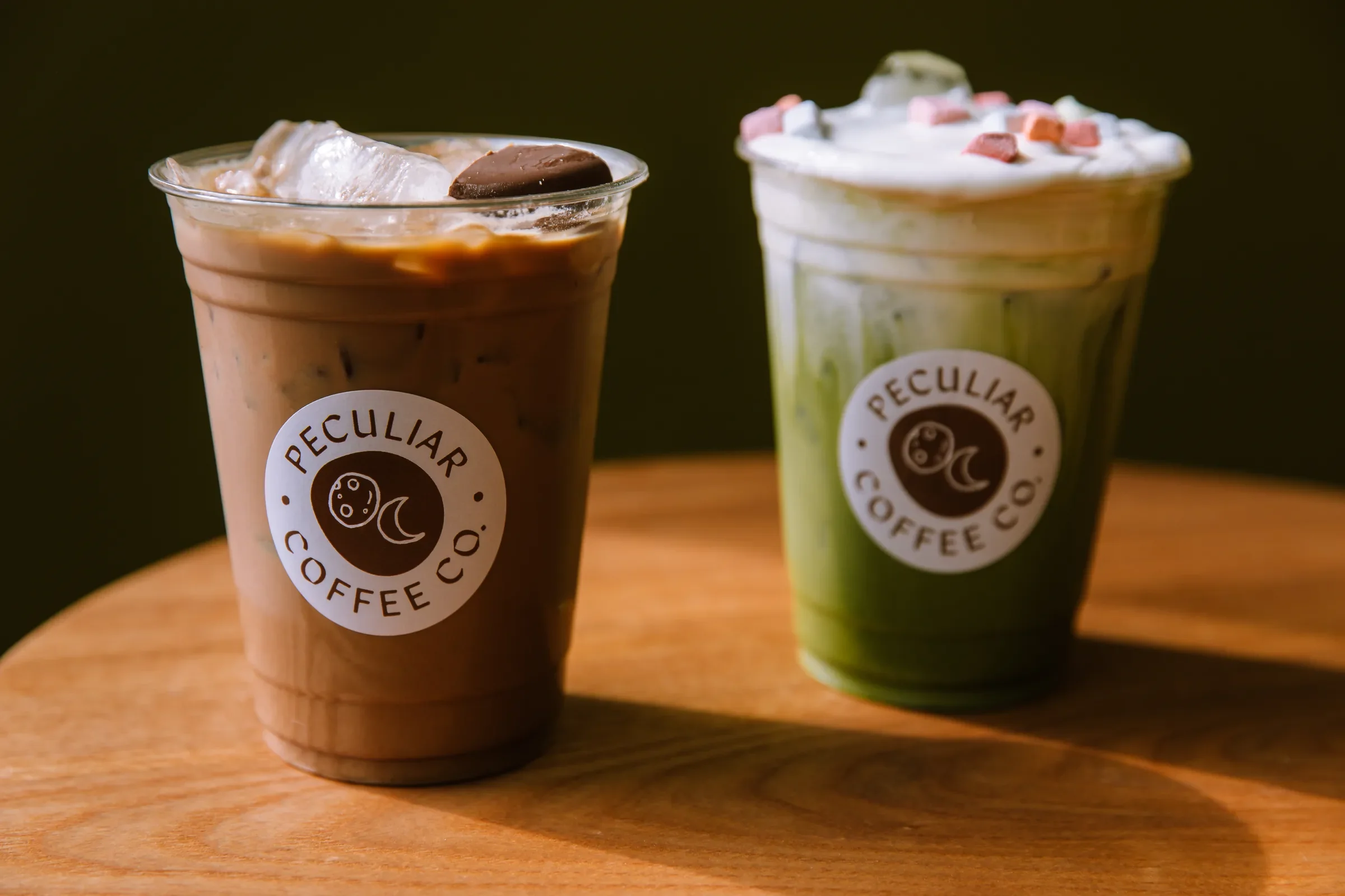 Two Peculiar Coffee signature drinks, an iced mocha and a marshmallow matcha, in branded cups