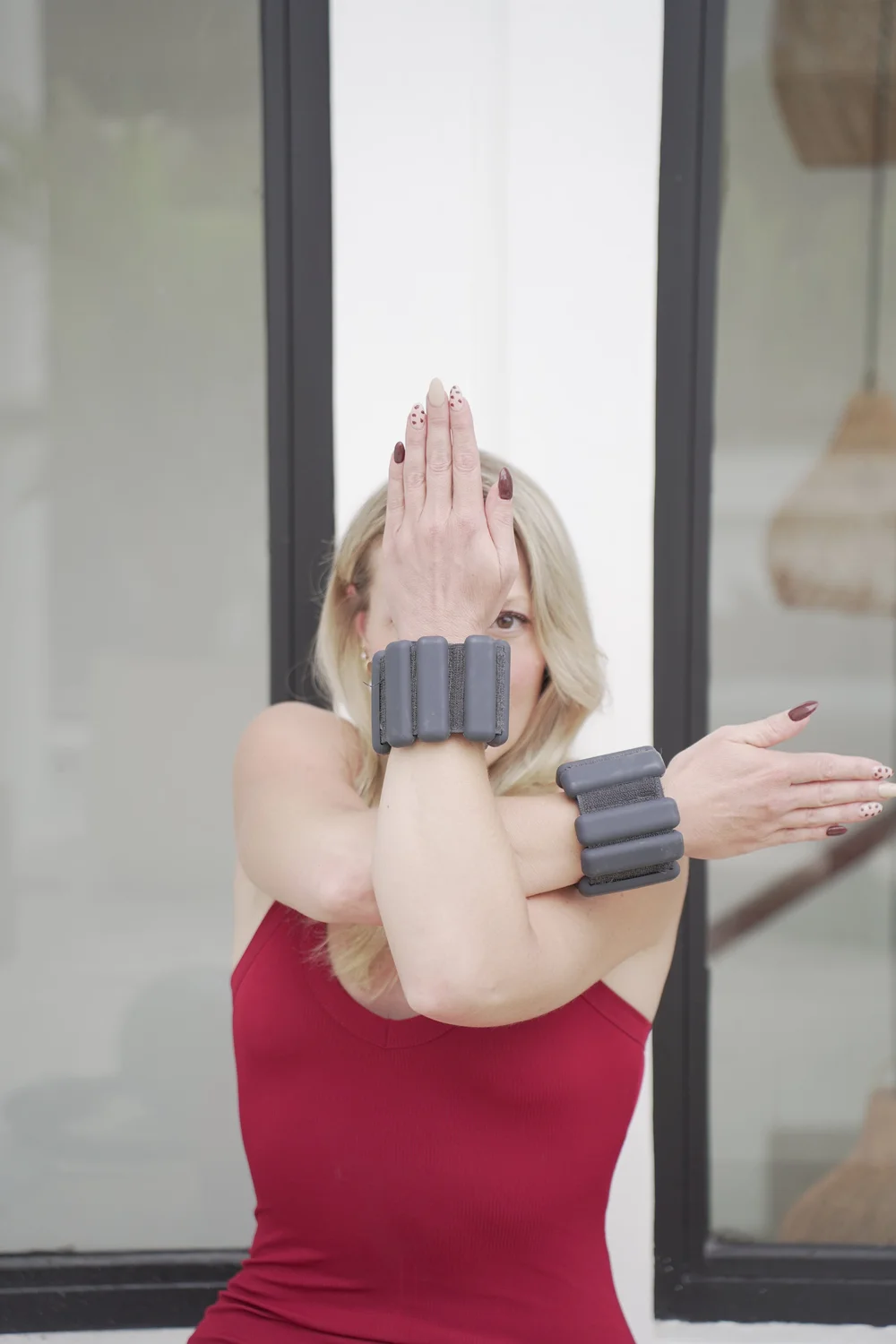 Emilie in a red top, arms wrapped in front of her face in eagle arms, wearing wrist weights