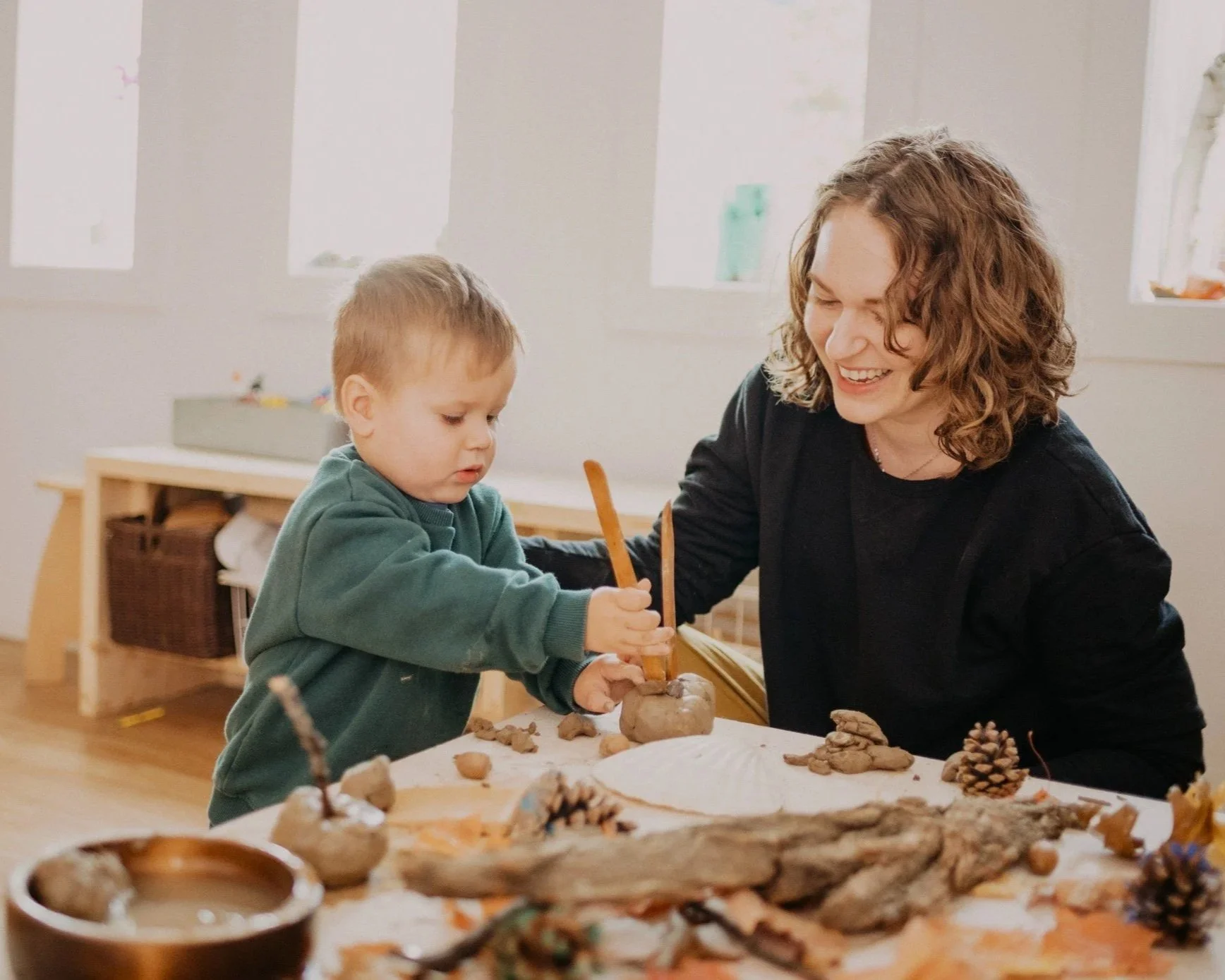 A child and an educator exploring clay and natural materials together.