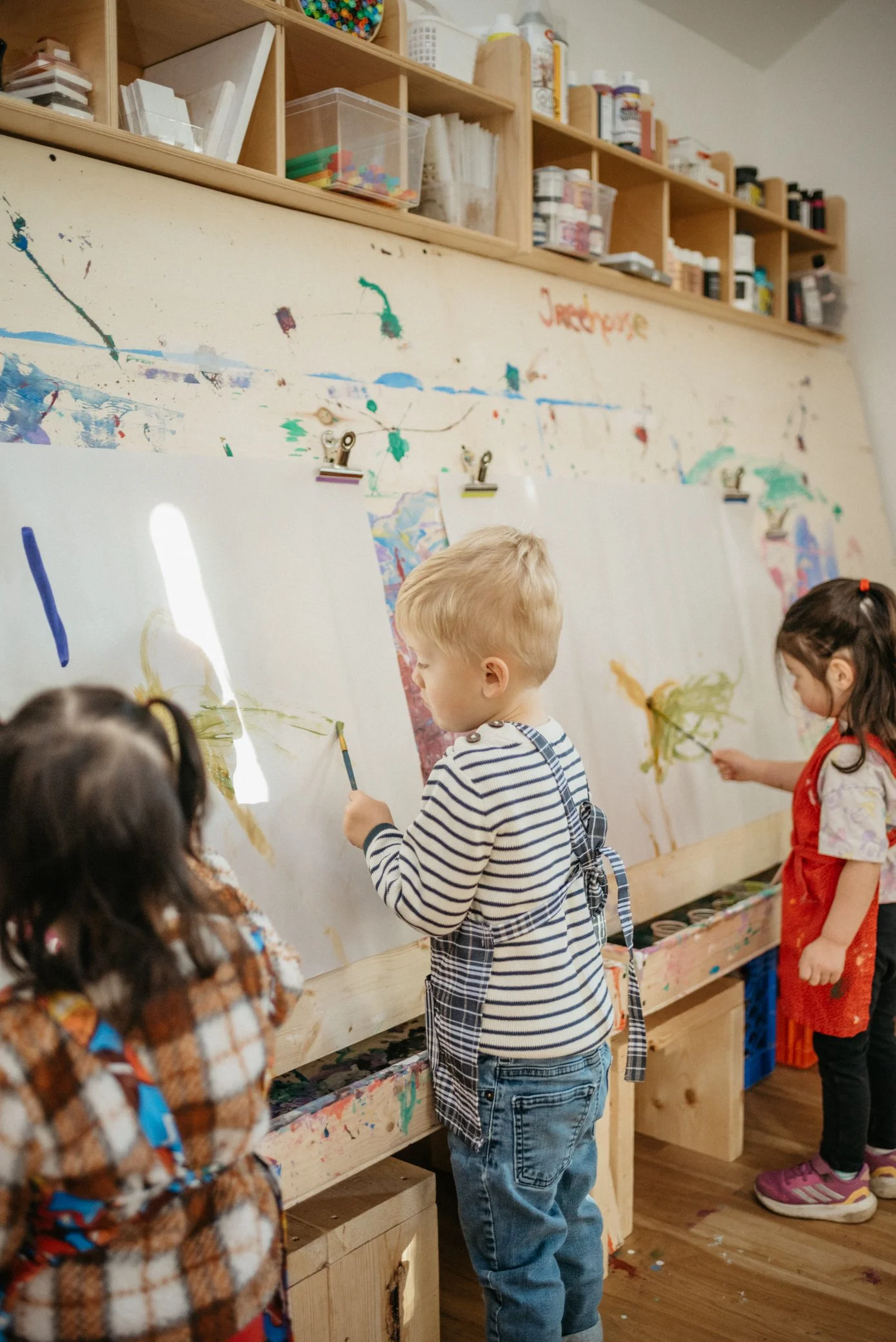Children painting at the studio's easel wall