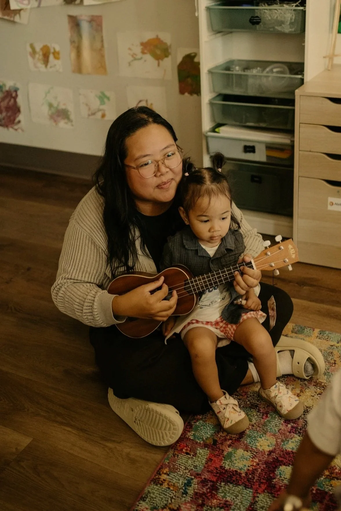 An educator and a young child playing a ukulele together.