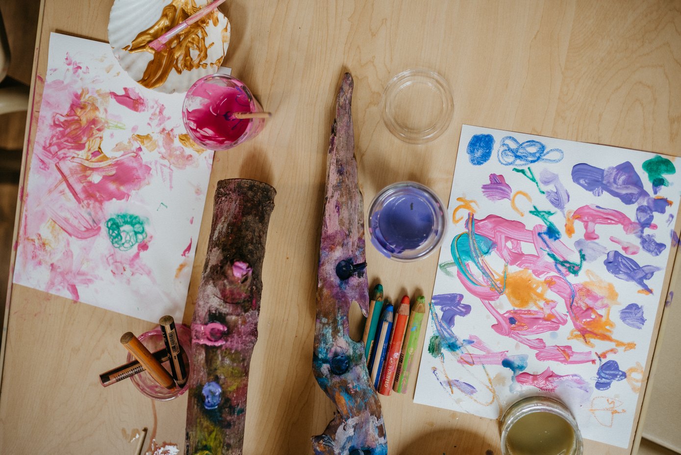 Paints, natural materials, and children's artwork on a studio table
