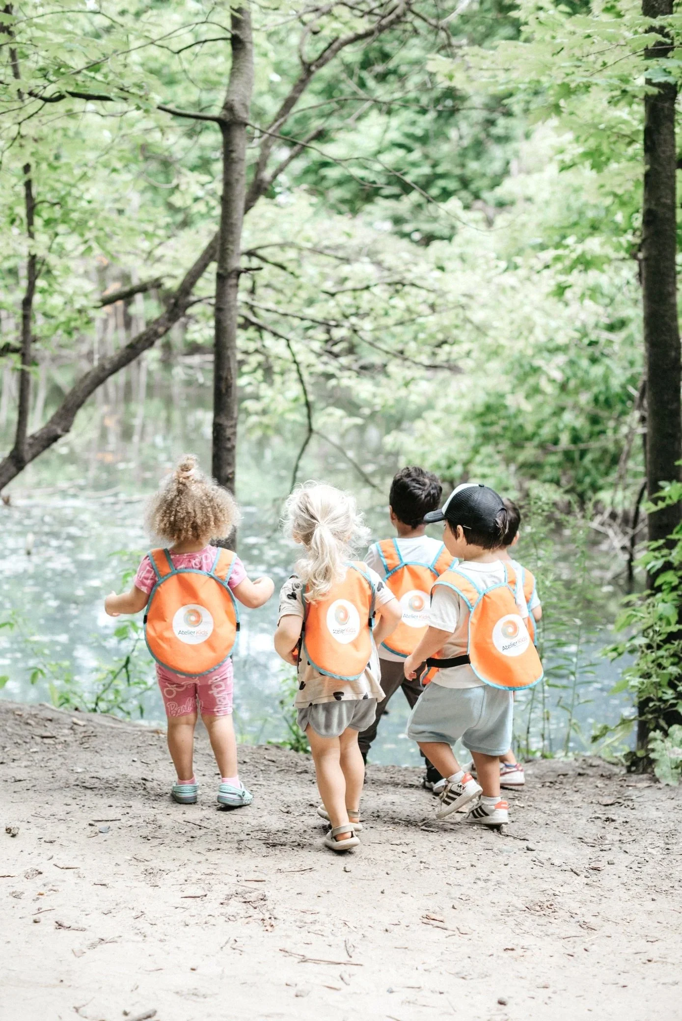 Children with backpacks walking a forest trail toward a pond