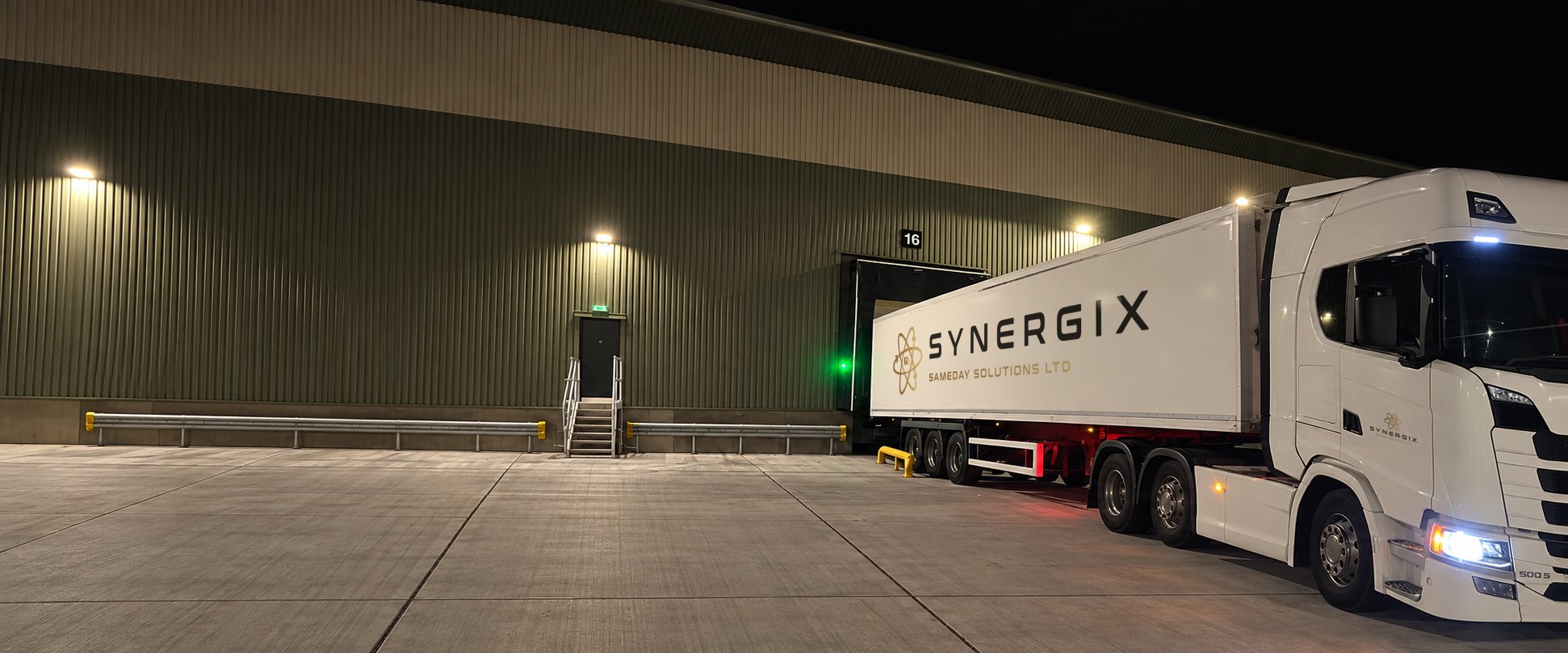 Synergix-branded articulated lorry at a warehouse loading bay at night