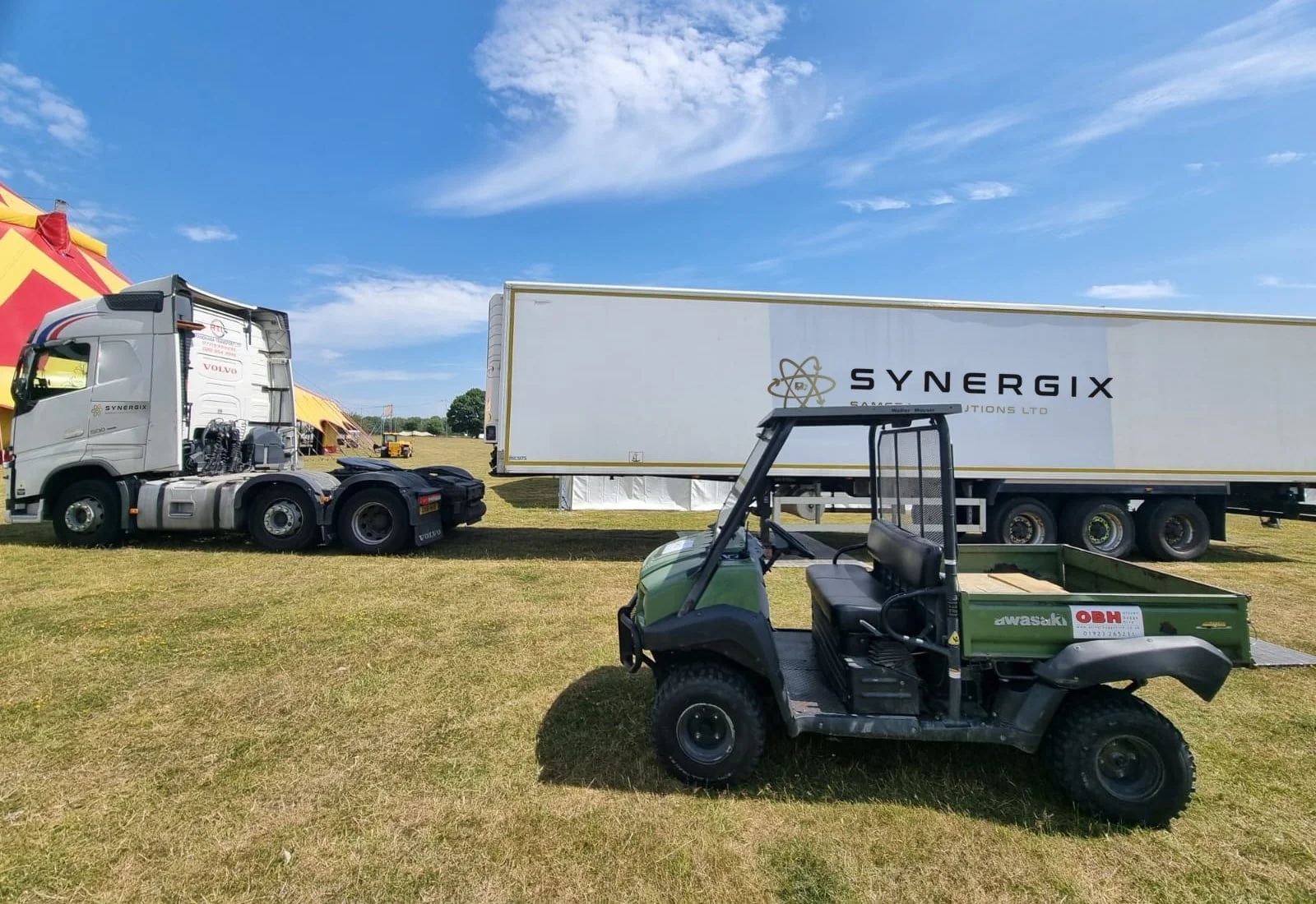 Synergix-branded tractor unit and trailer at an outdoor event site with a utility buggy.
