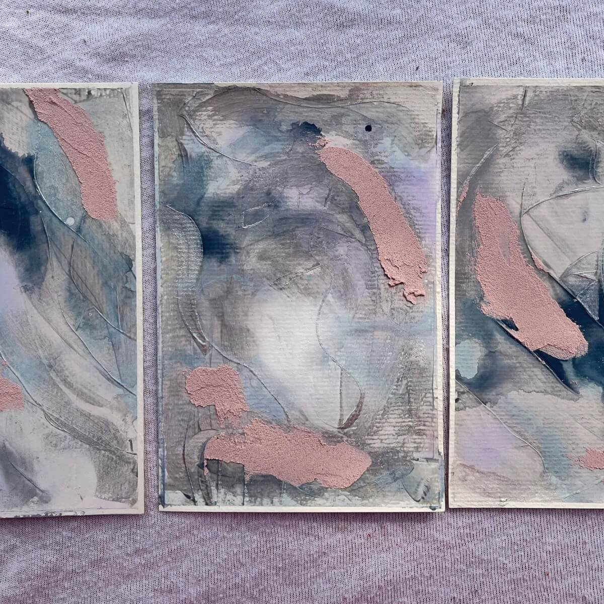 Three artworks from the “Between Breaths” series – flowing blues, greys and blush tones on textured surfaces, inspired by emotional clarity and inner calm.