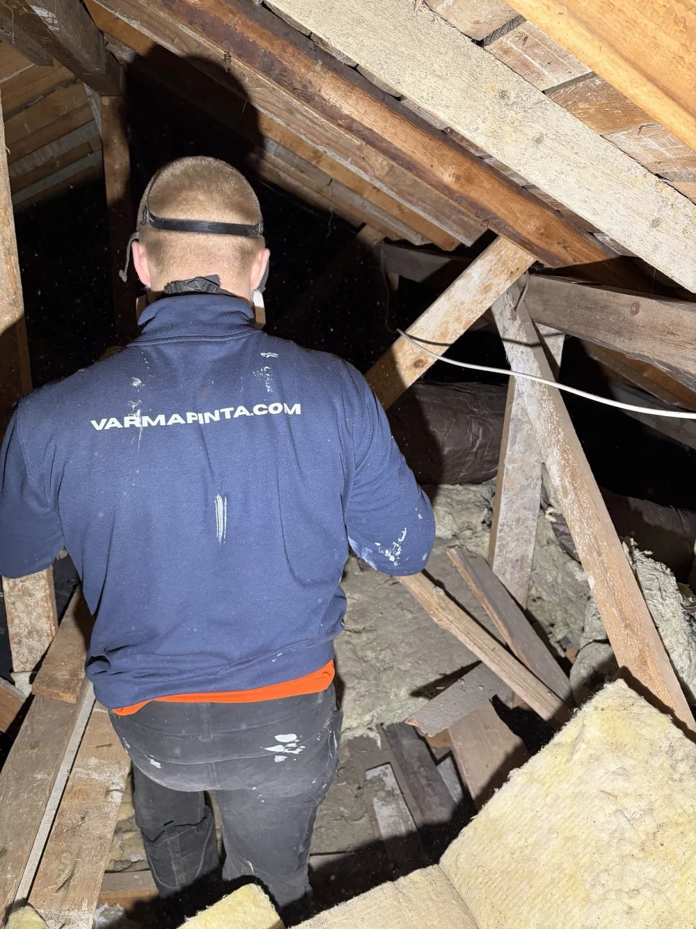Asentaja yläpohjassa vanhojen eristeiden keskellä saneerauksen alussa