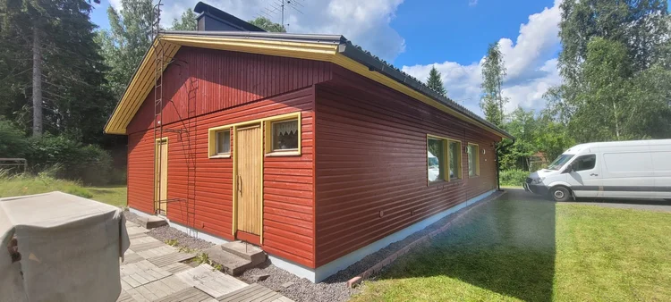 Punainen puutalo maalauksen jälkeen, kirkas punainen ja keltaiset listat
