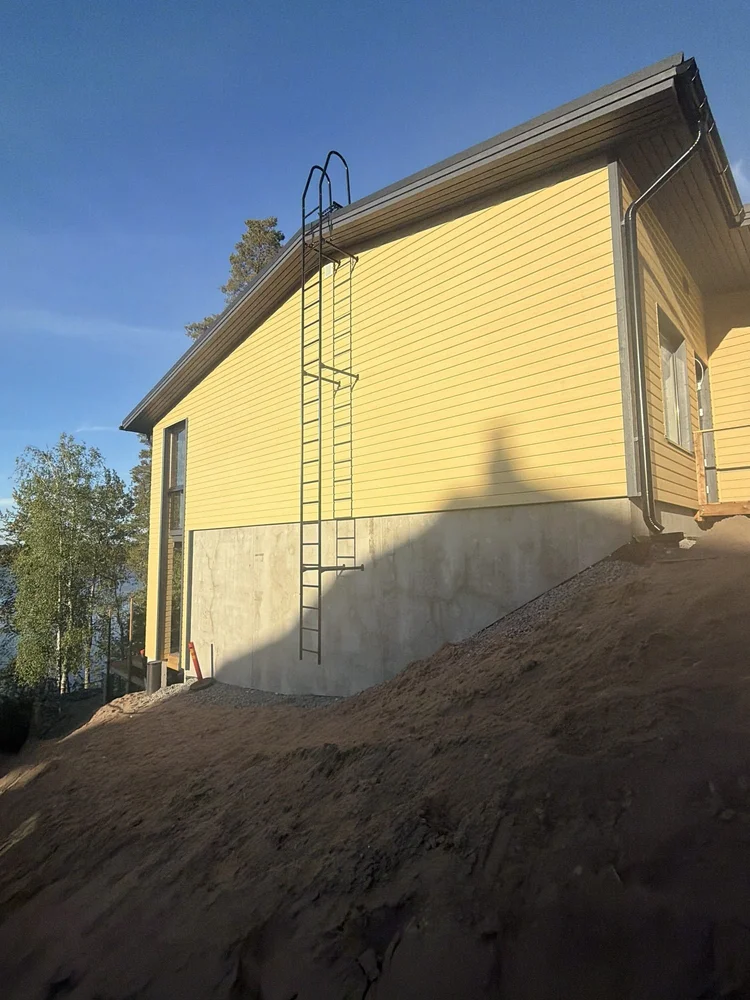 Keltainen julkisivu ja kattotikkaat järvenrannassa