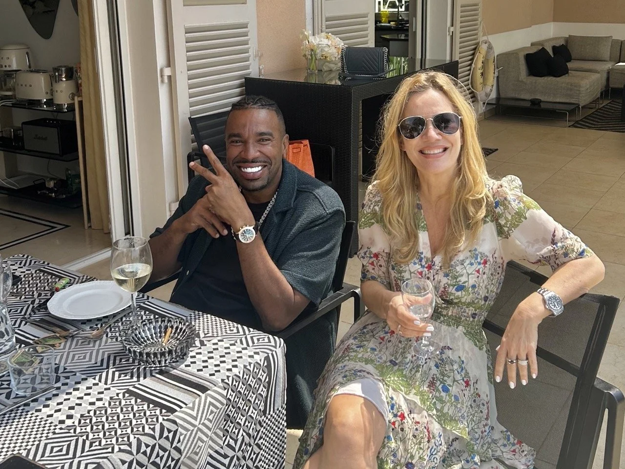 American rapper and Drink Champs podcast co-host N.O.R.E. seated at an outdoor dining table at Villa Monaco with owner Jessica Stockmann, both with a glass of white wine
