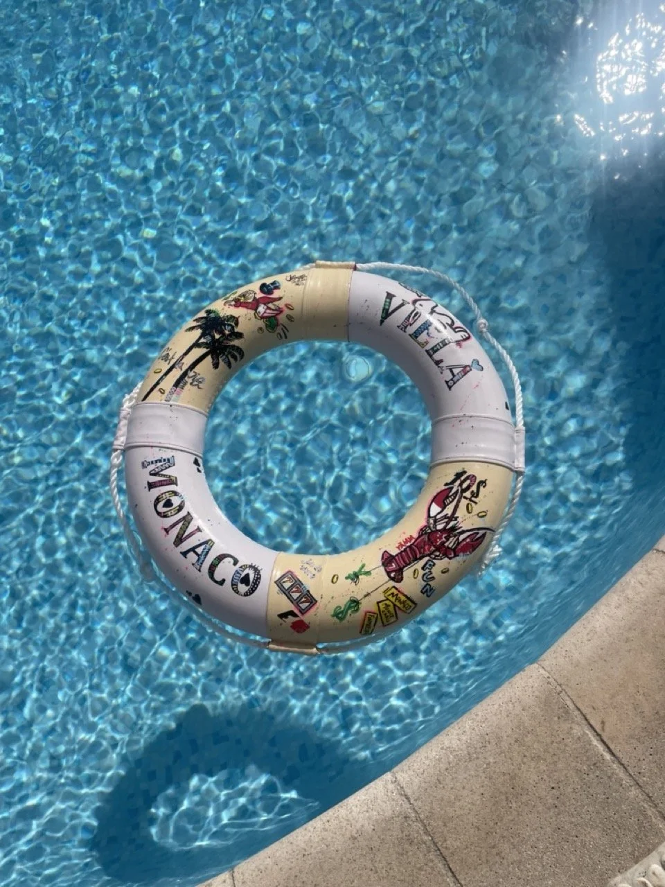 A custom illustrated Villa Monaco life ring floating in the villa's pool, hand-decorated with palm trees, a red lobster and other Monaco motifs