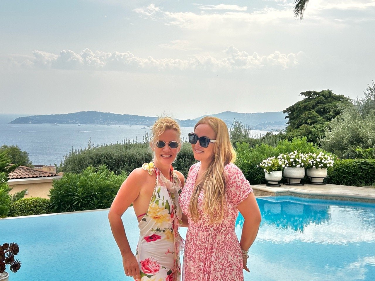 French singer Hélène Ségara and Villa Monaco owner Jessica Stockmann standing together by the villa's infinity pool, with the Mediterranean sea view stretching toward Cap Ferrat behind them